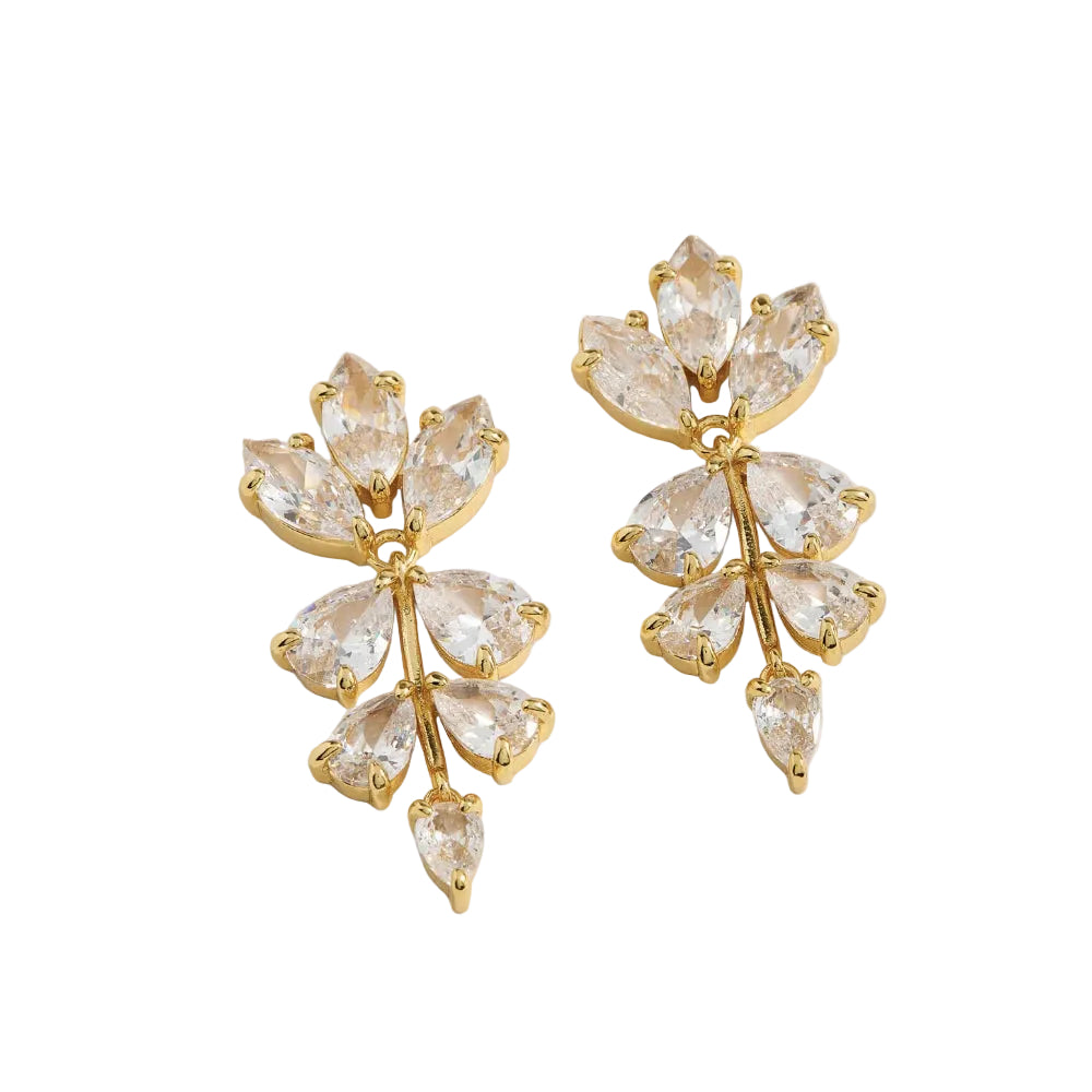 A pair of gold-toned statement earrings featuring marquise and teardrop-cut clear crystals arranged in a leaf or floral cluster design, set against a light beige background.