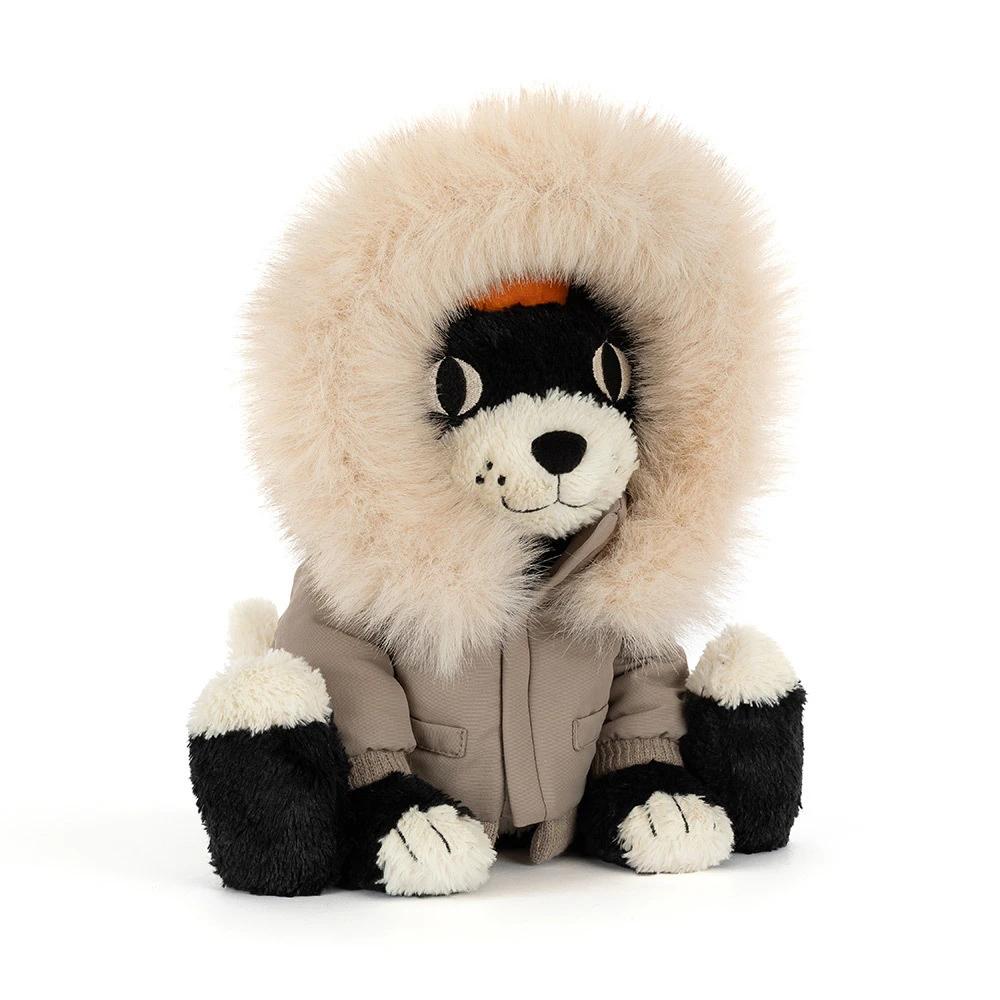 A plush dog toy wearing a beige parka with a large cream faux-fur hood and black-and-white paws and face, photographed on a clean white background.