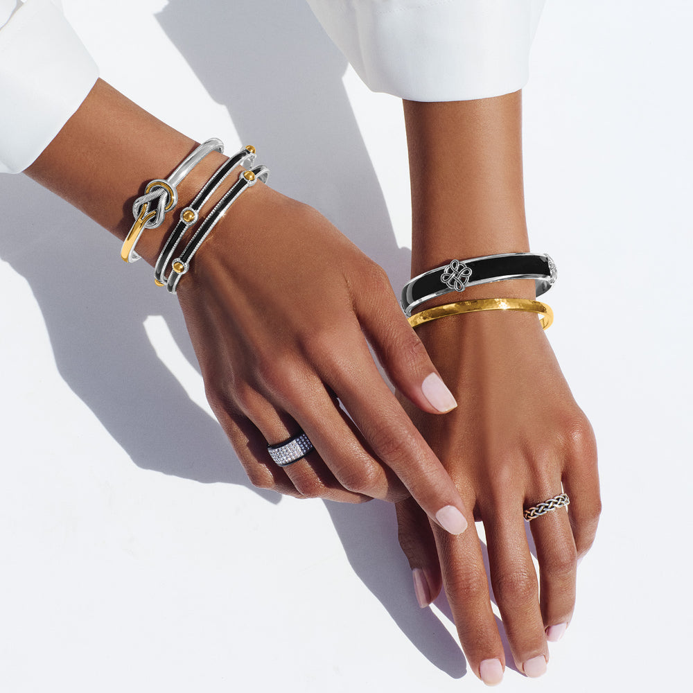 Hands wearing multiple bracelets and rings on a white background