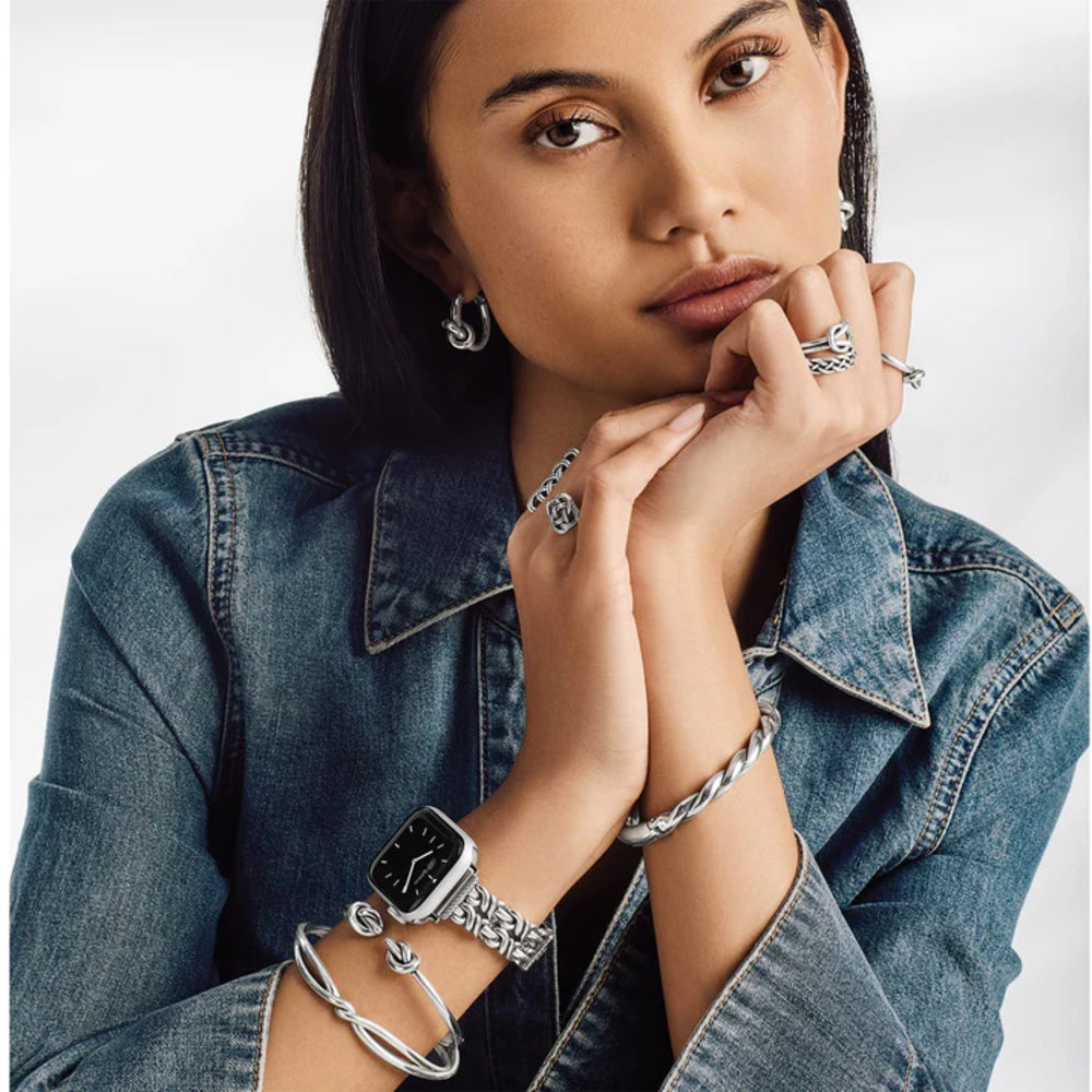 Woman wearing multiple silver bracelets and rings on a plain background