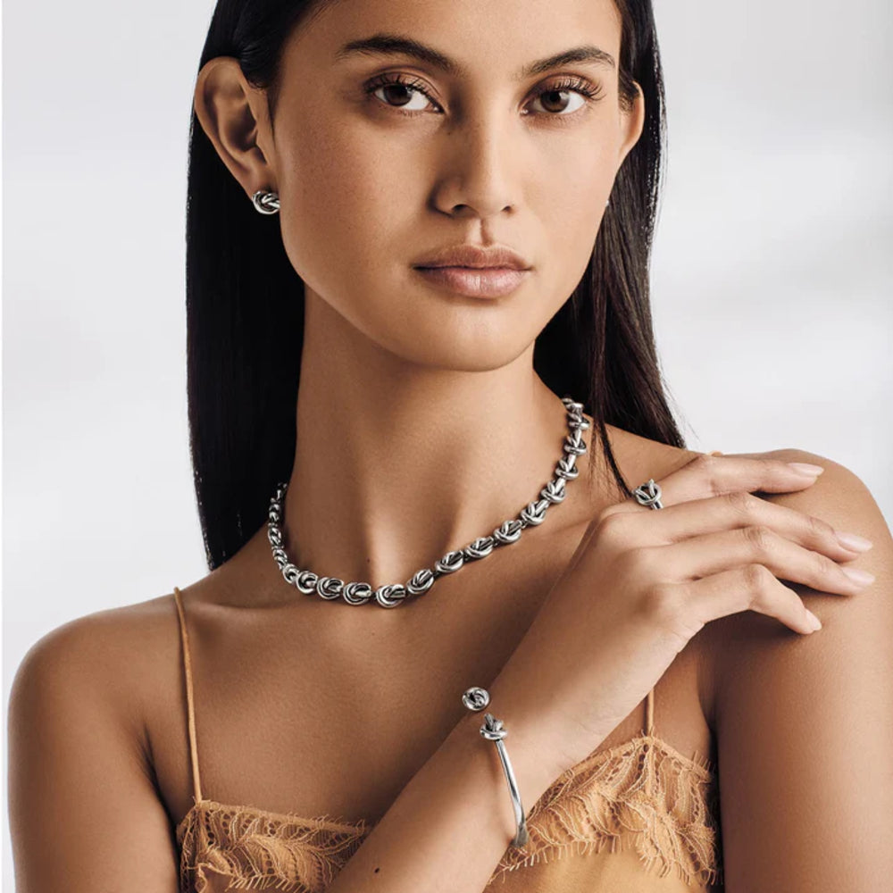 Woman wearing silver jewelry including a necklace, earrings, and bracelet on a plain background