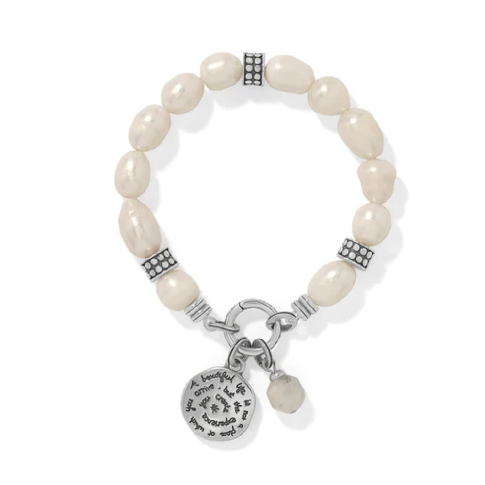 A beaded stretch bracelet featuring irregular cream-colored beads, silver-toned spacer accents, and a dangling round silver charm engraved with 'Love is patient, love is kind.