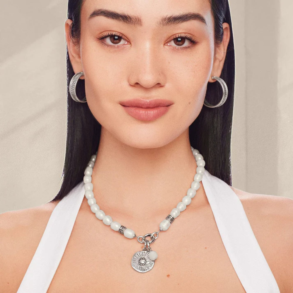 Woman wearing a pearl necklace and hoop earrings against a neutral background