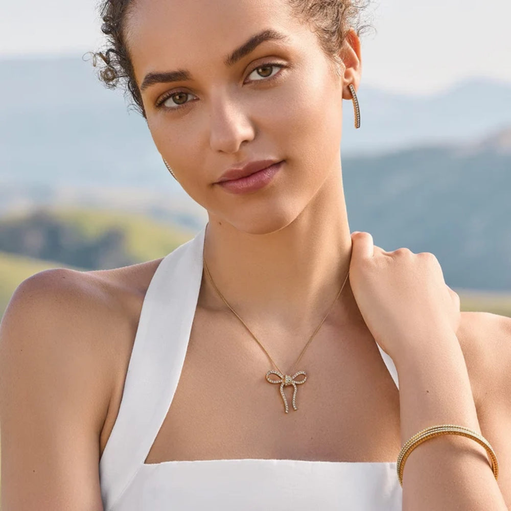 Woman wearing a gold necklace and earrings with a scenic background