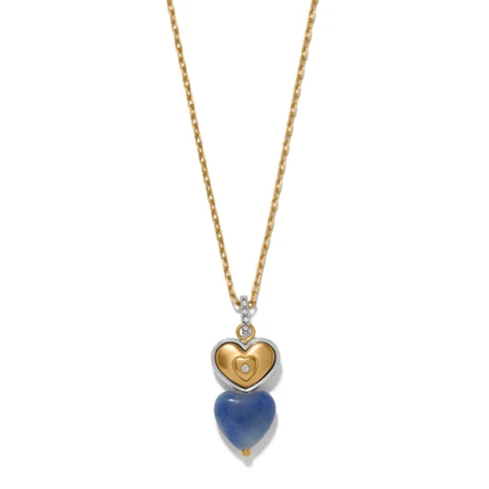 A gold heart pendant necklace with a silver heart containing a small white stone, and a dangling blue heart stone below, shown on a white background.