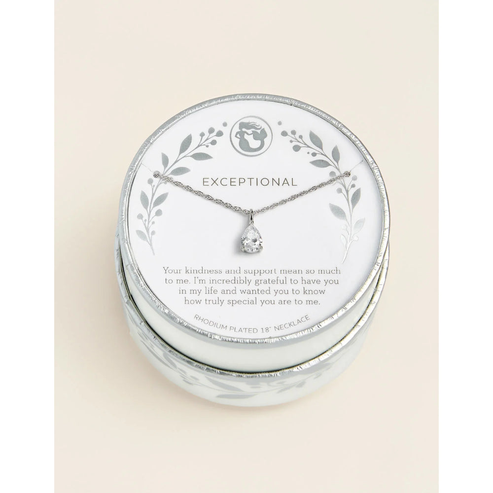 A silver necklace with a clear teardrop-shaped gemstone pendant, presented on a round white card inside a round silver gift box. The card features a silver leaf border, the brand name 'EXCEPTIONAL', and a sentimental message printed on it, all set against a solid cream background.