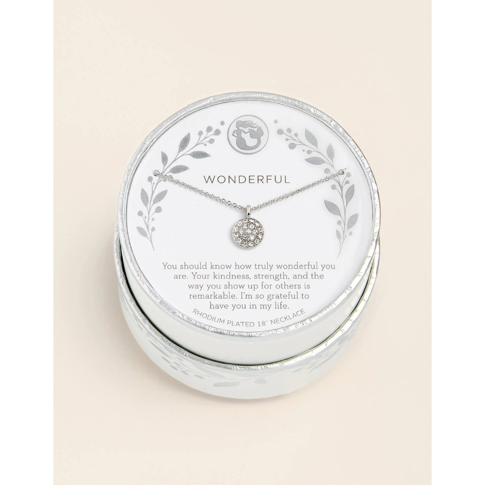 A silver necklace with a round clear gemstone pendant displayed on a white circular card inside a silver round gift box. The card is printed with the word 'WONDERFUL' and a sentimental message, set against a light beige background.
