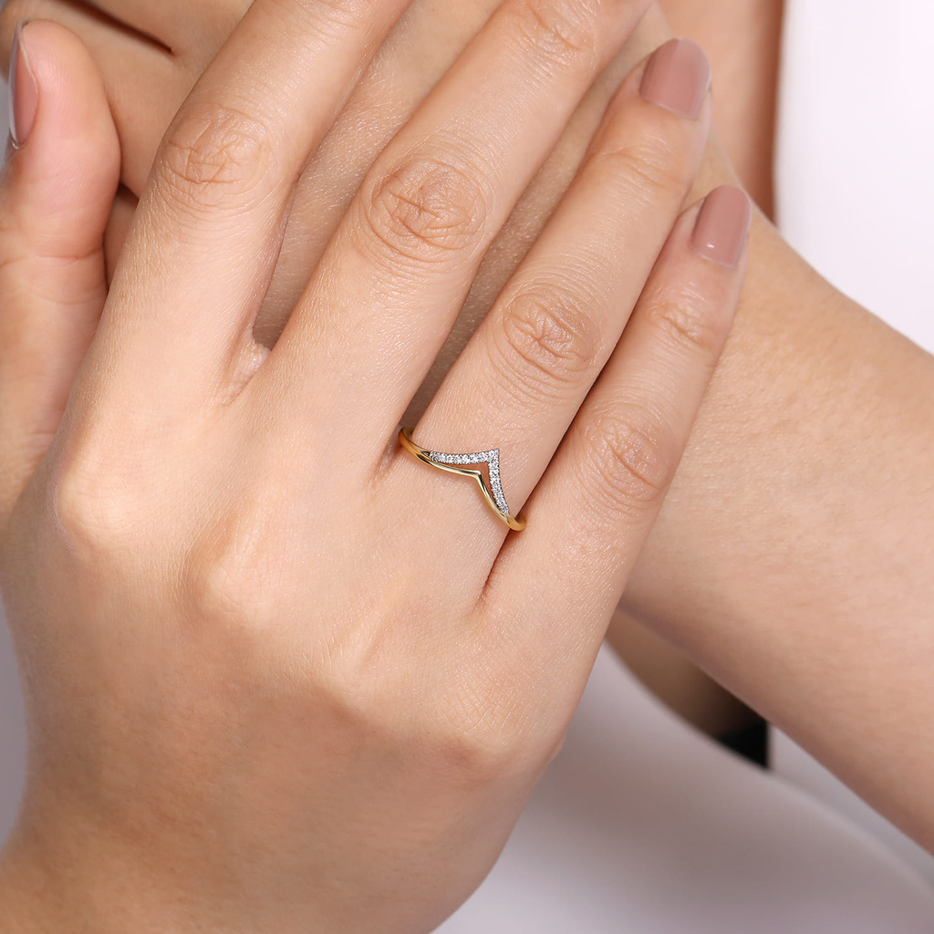 Gold ring with a diamond on a person's finger against a neutral background