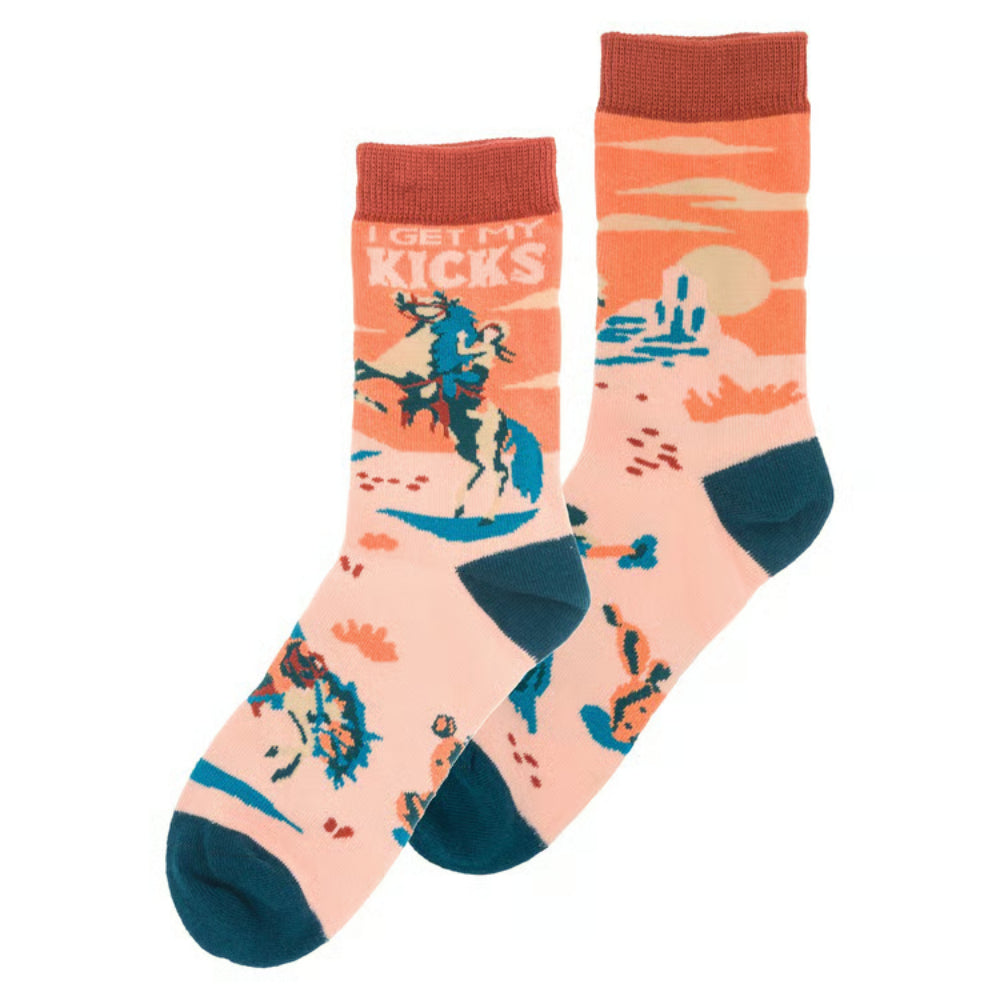 A pair of crew socks with a retro western desert theme. The socks feature a light peach-pink base with orange, teal blue, and dark brown graphics, including a cowboy on a bucking horse and the text 'I GET MY KICKS'.