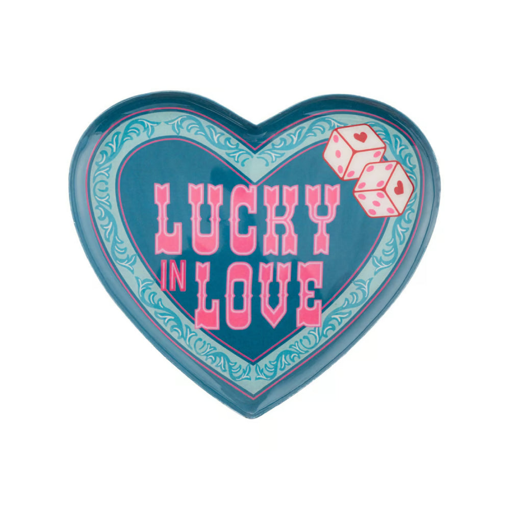 A heart-shaped decorative sign or plaque featuring the words 'LUCKY IN LOVE' in pink lettering, with two pink dice at the top right, on a light blue patterned background with a darker blue border.