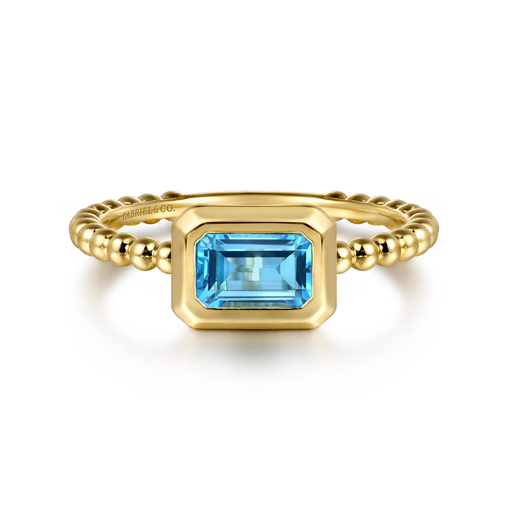Gold ring with a blue gemstone on a pink cushion
