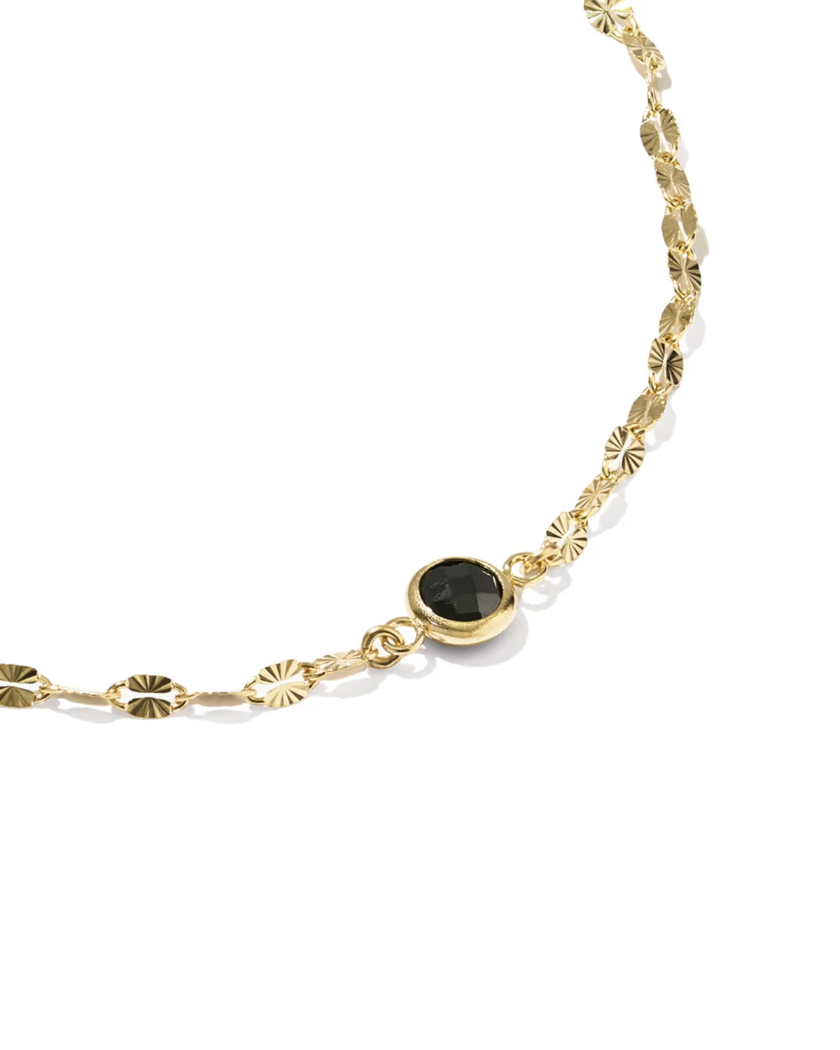 A gold chain bracelet featuring textured sunburst link motifs and a central round bezel-set black gemstone, photographed on a clean white background.