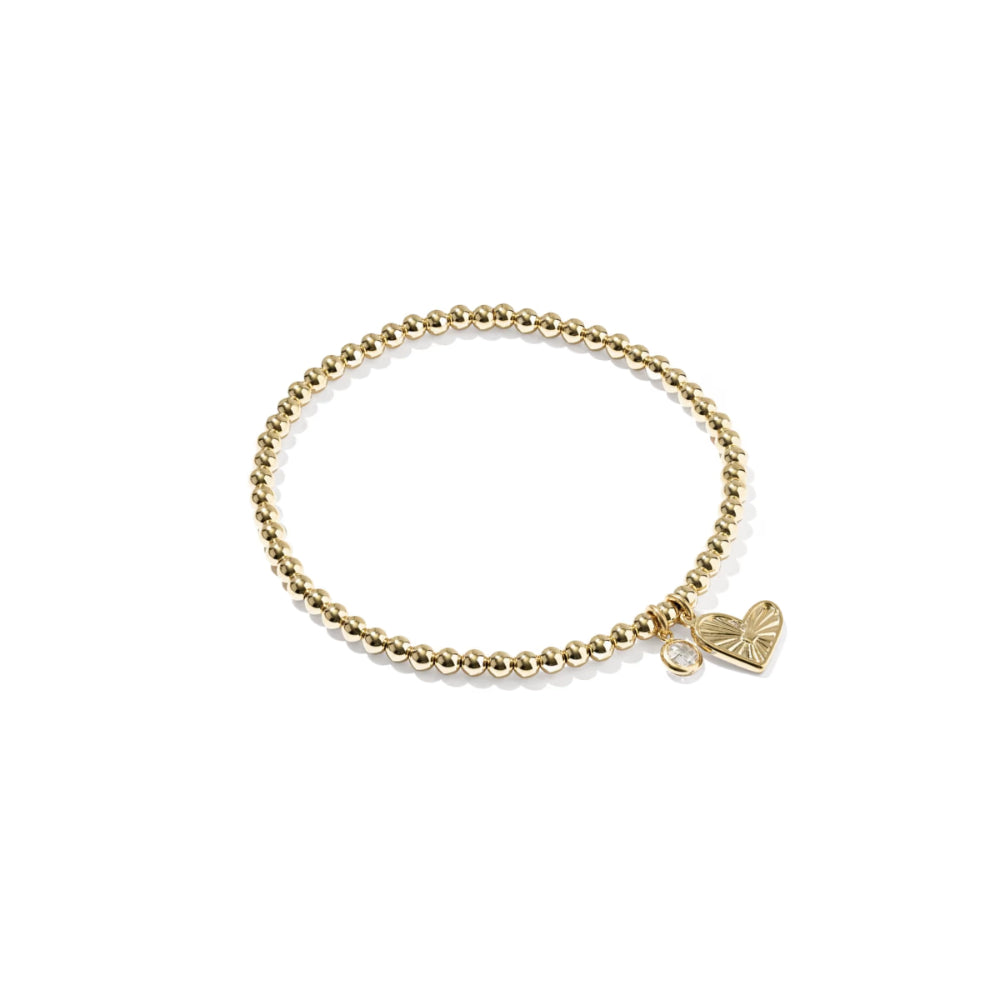 A gold beaded stretch bracelet with a small heart-shaped charm featuring a bow design, displayed on a clean white background.
