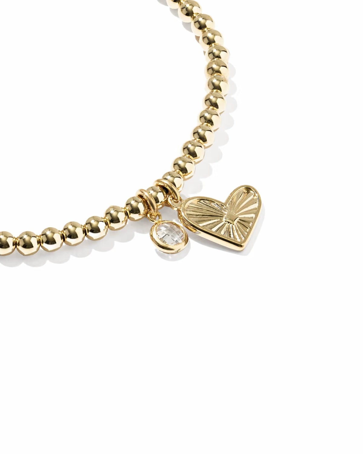 A gold beaded stretch bracelet featuring a textured heart charm and a small clear crystal bead, shown on a clean white background.