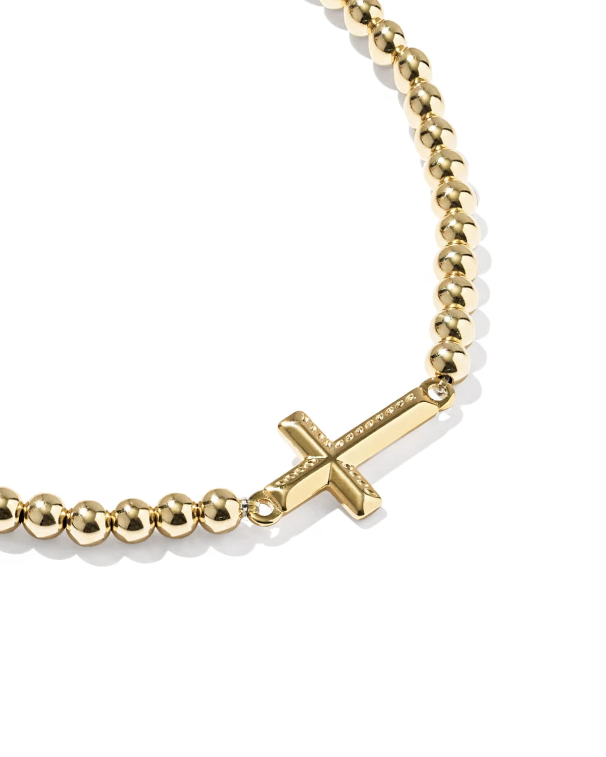 A close-up of a gold bead bracelet featuring a small cross charm, set against a clean white background.