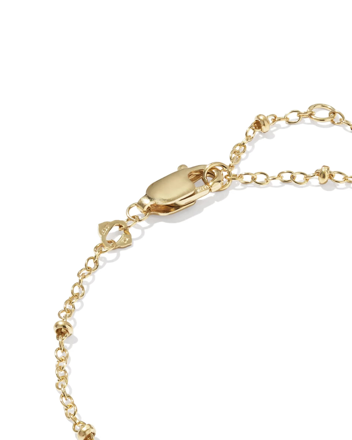 Close-up detail of a gold chain bracelet showing a lobster clasp, a small bow charm, and a beaded section on a clean white background.