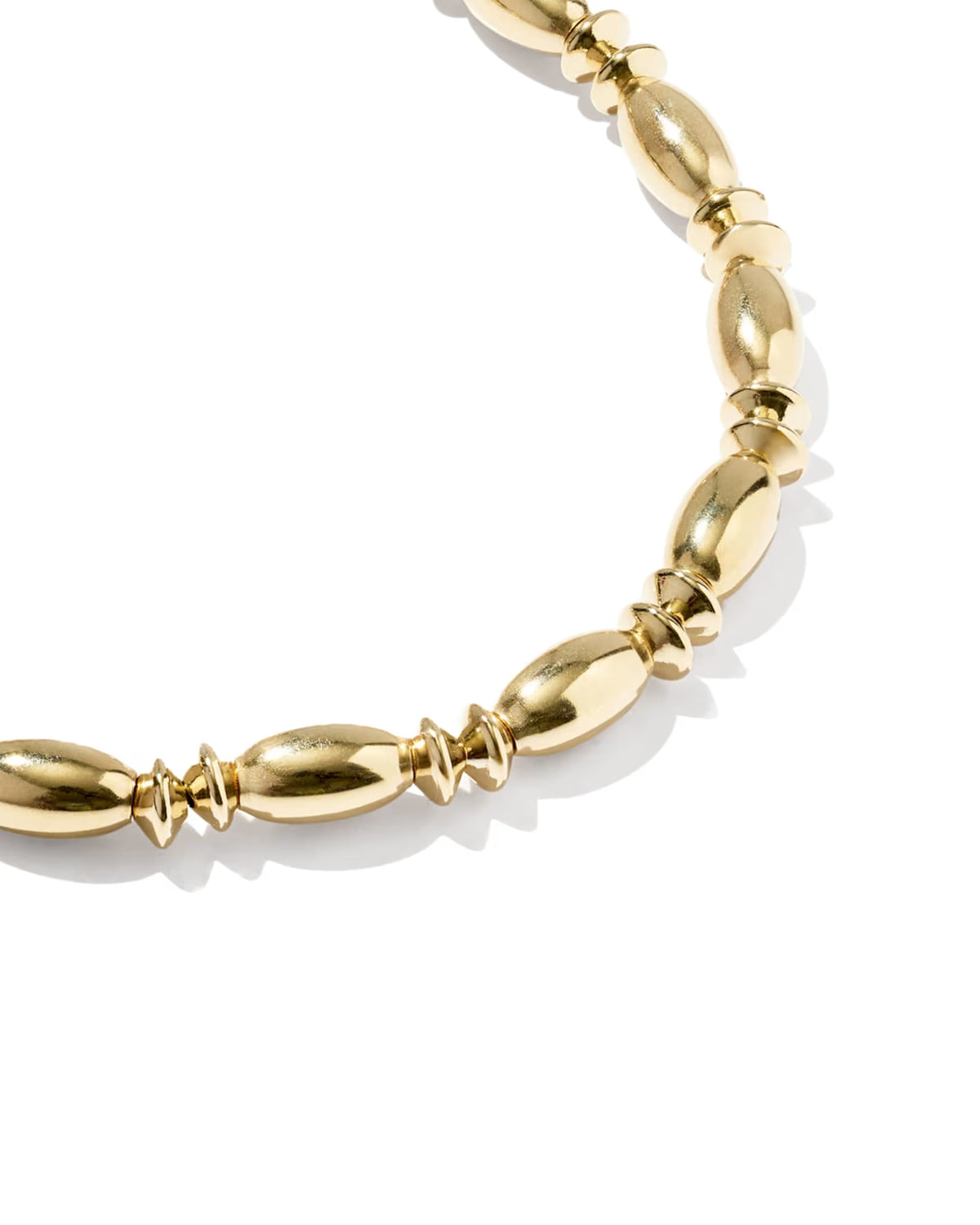 A close-up of a gold beaded stretch bracelet with elongated oval beads and smaller twisted spacer beads, photographed on a clean white background.