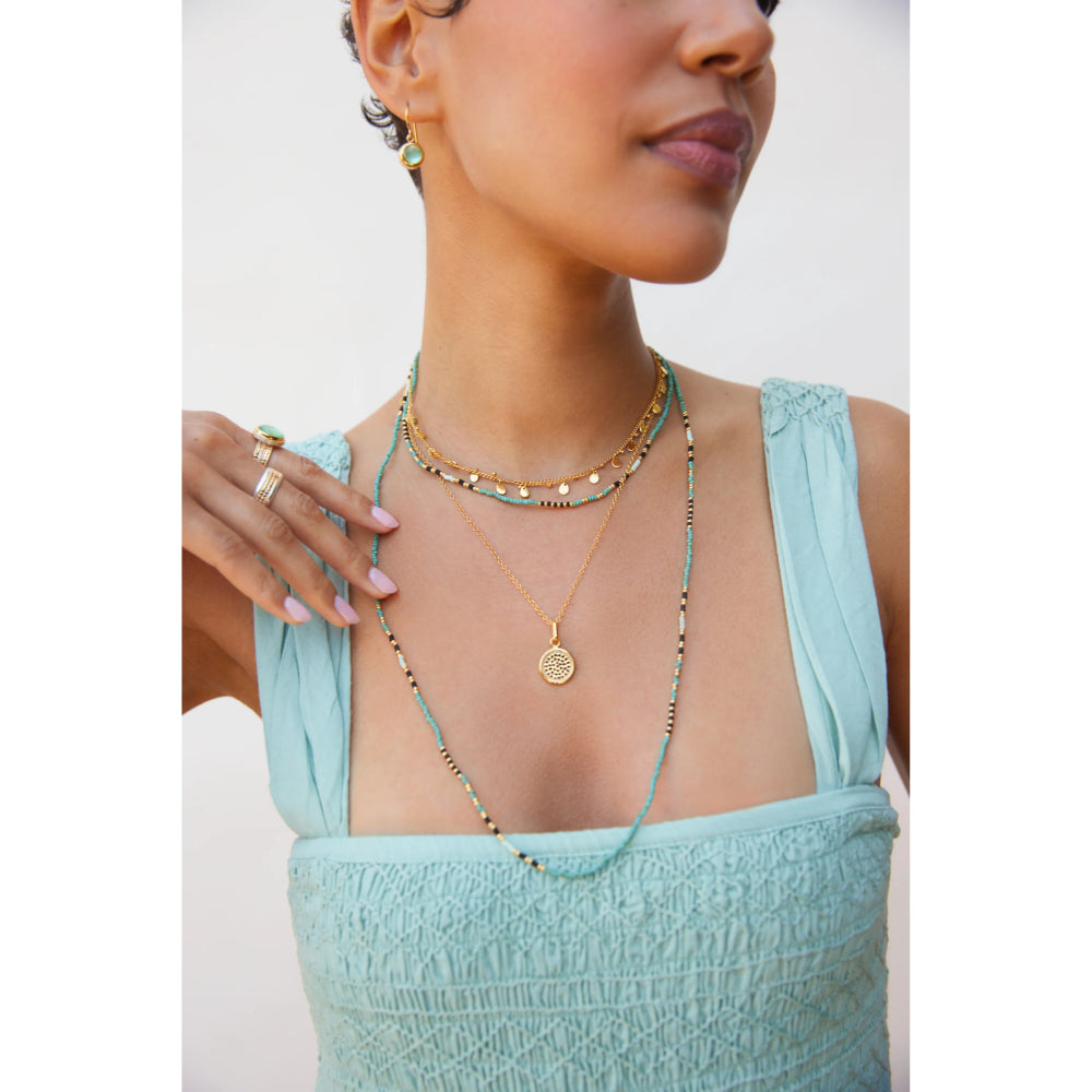 Woman wearing a light blue top and multiple beaded necklaces