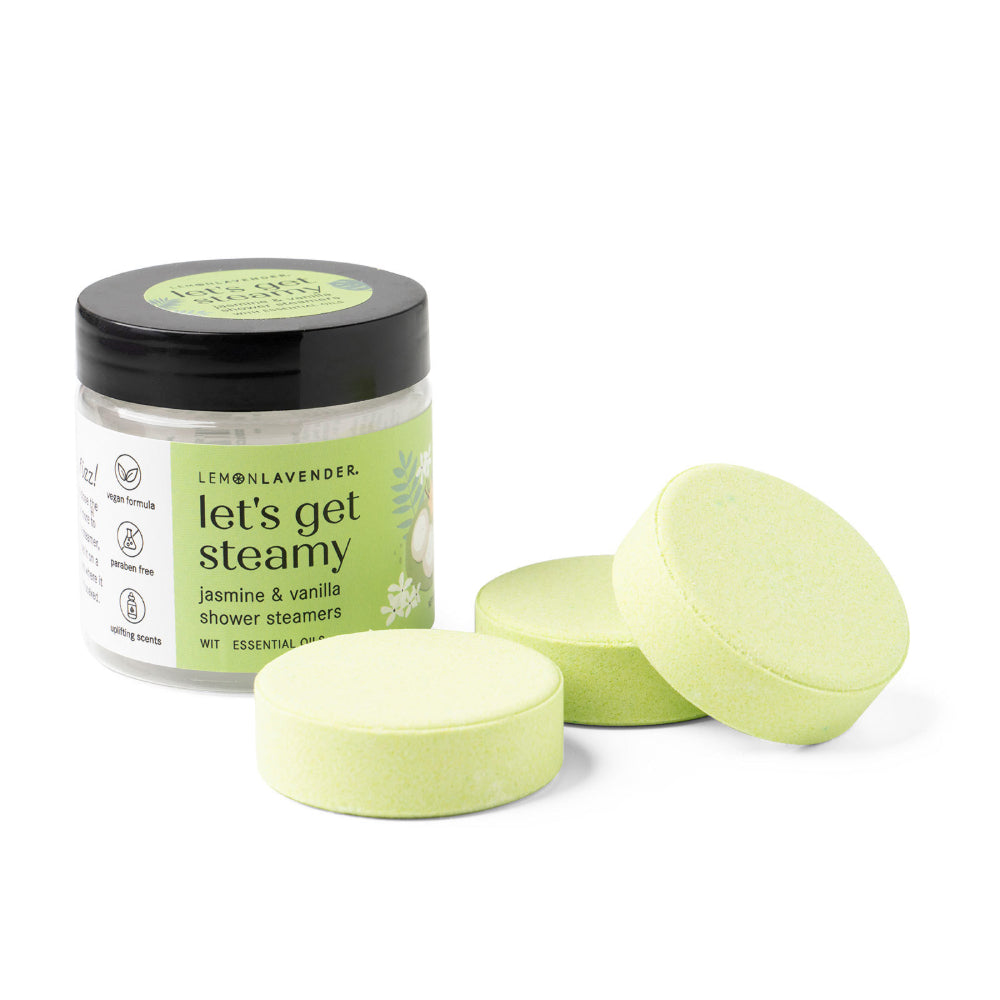 Jar of 'let's get steamy' shower steamers with three green tablets on a white background