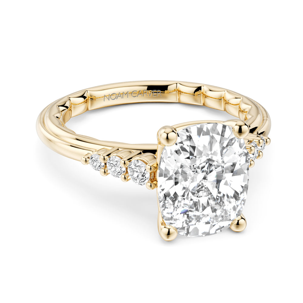 Gold Noam Carver ring with a large elongated cushion diamond and smaller diamonds on the band against a white background
