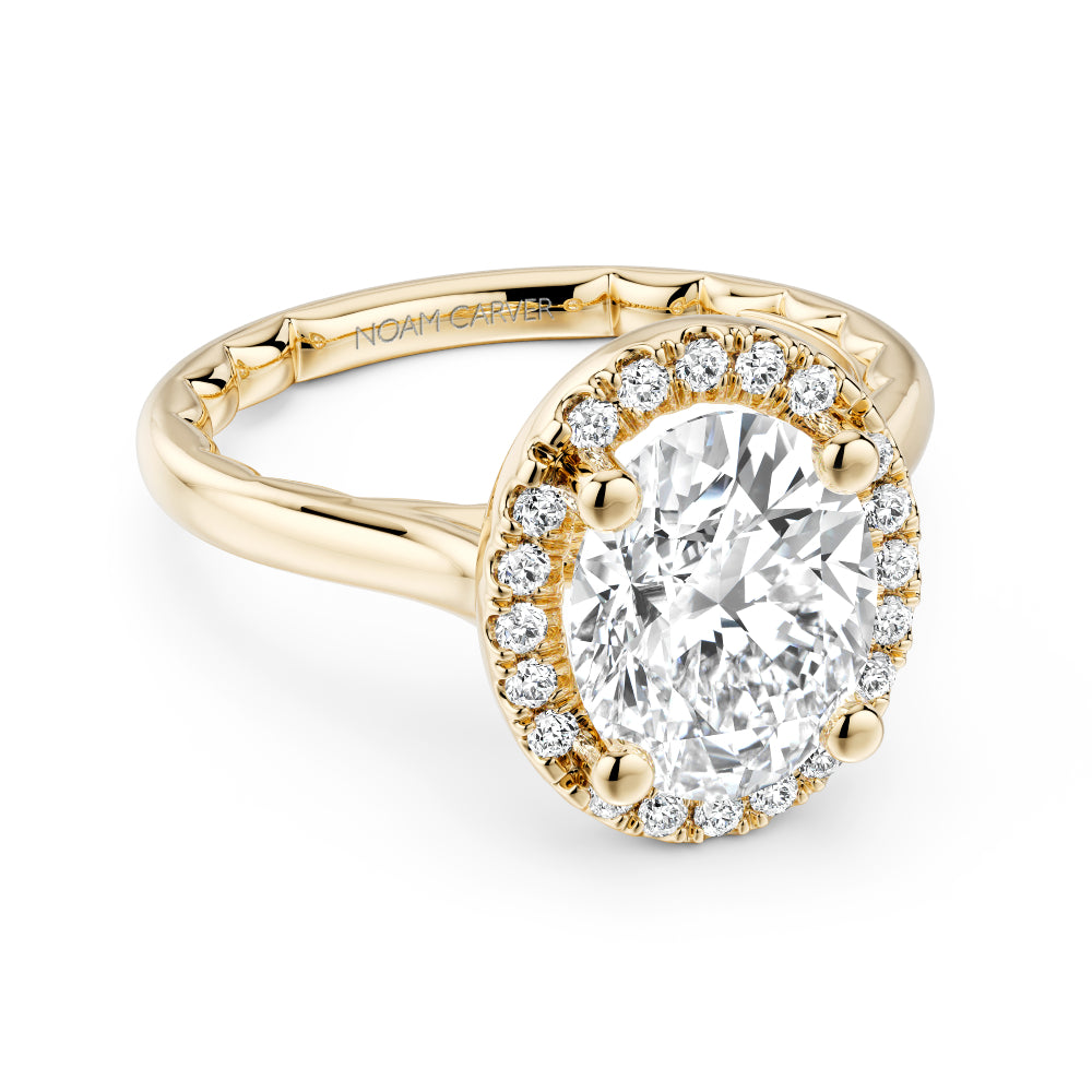 Gold Noam Carver ring with a large oval diamond center and smaller round diamond sides on a white background