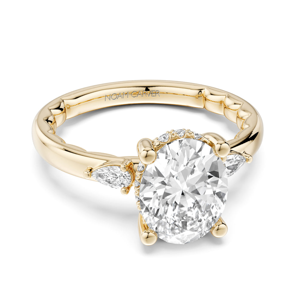 Gold Noam Carver ring with a large oval diamond center and smaller pear shape diamond sides on a white background