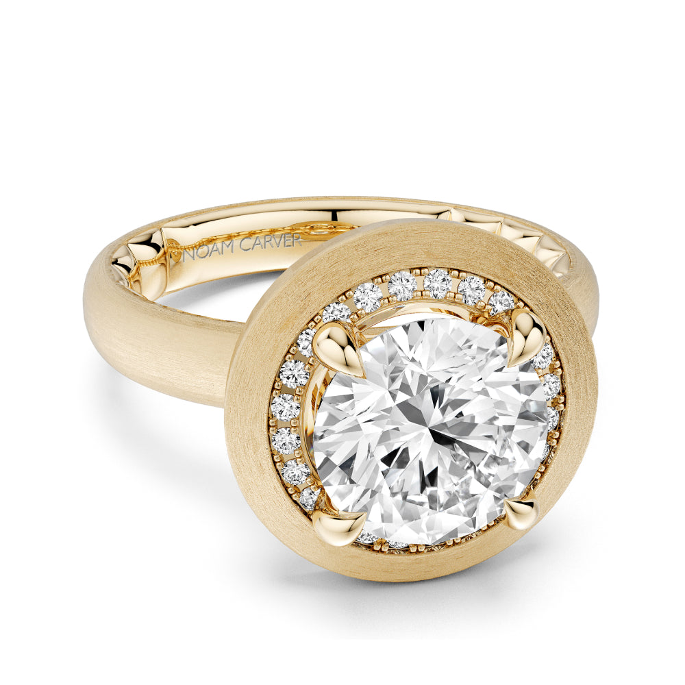 Brushed gold Noam Carver ring with a large diamond and smaller surrounding diamonds on a white background