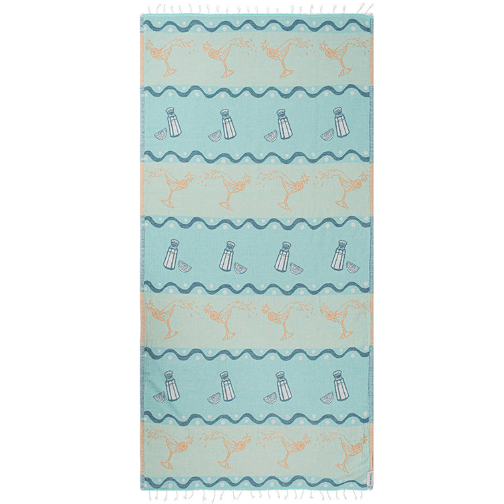Blue beach towel with beach-themed design featuring martini glasses and wavy lines with white tessal edges on a blue and beige background.