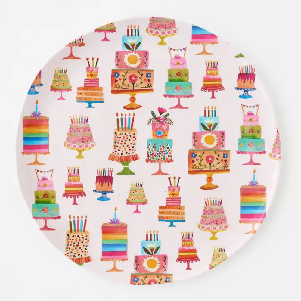 A round white plate featuring a colorful repeating pattern of illustrated birthday cakes on a light gray background.