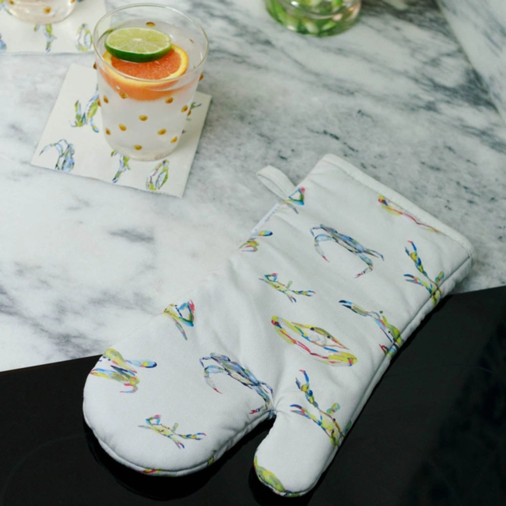 Oven mitt and pot holder with colorful Blue Crab pattern on a marble surface with a drink.
