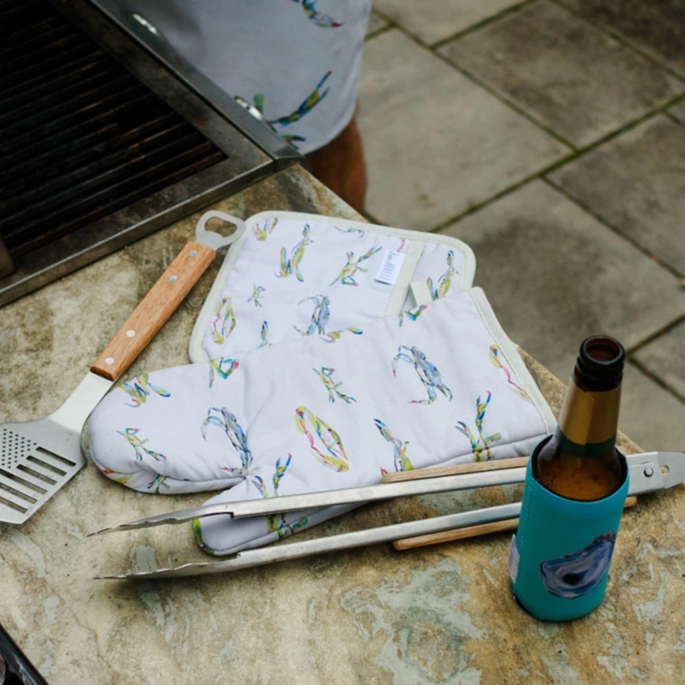Outdoor cooking scene with grill, oven mitts, bottle of beer, and tools on a stone surface.