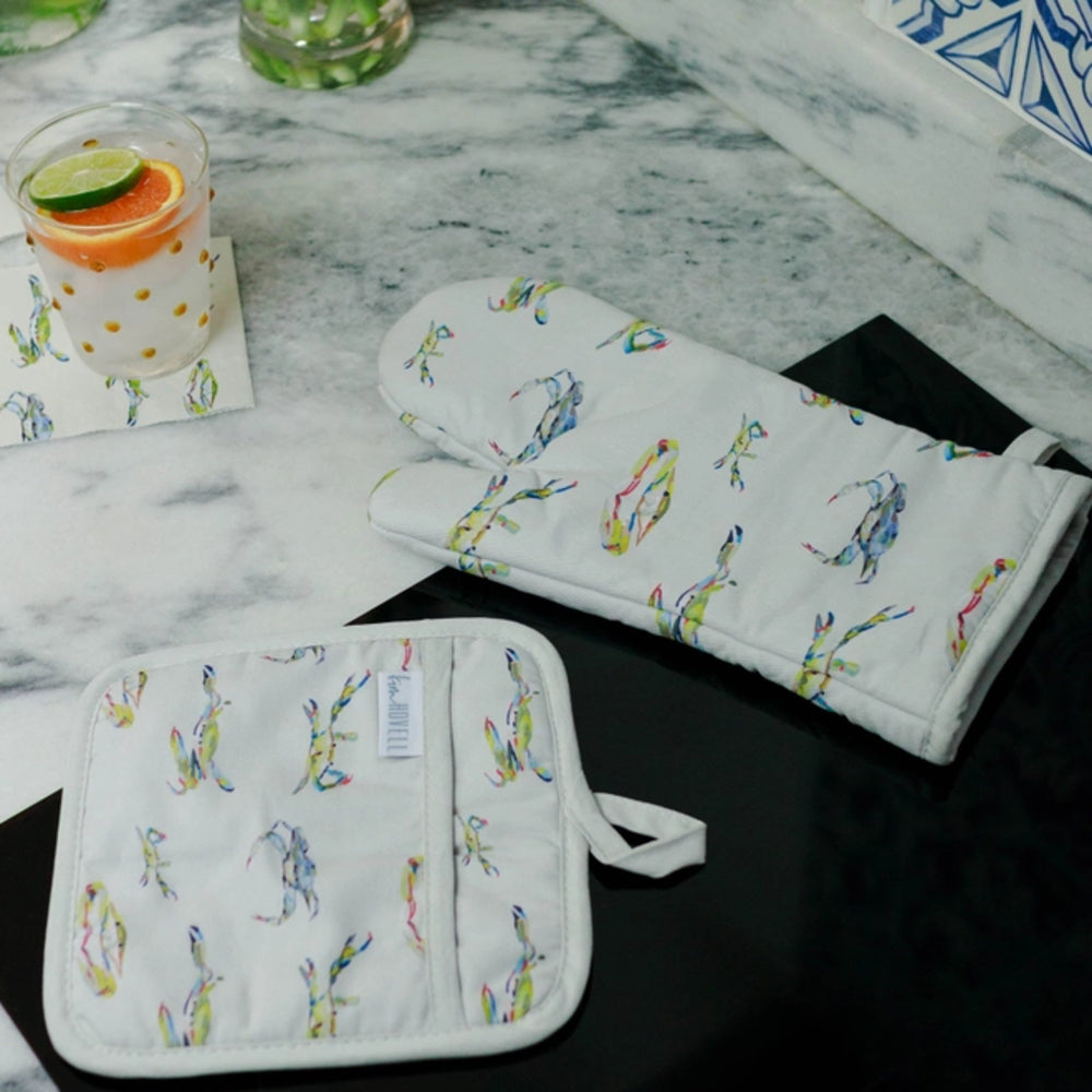 A white oven mitt and pot holder with colorful Blue Crab patterns on a marble surface.