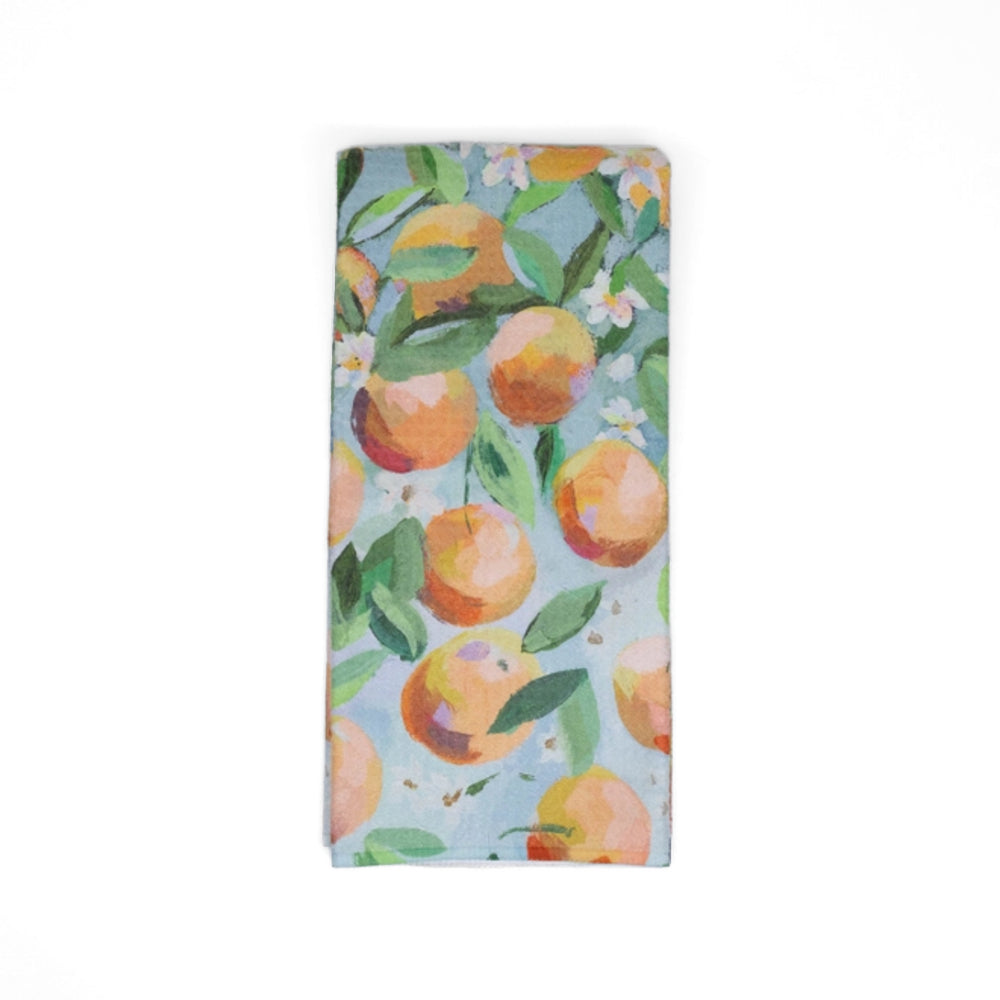 Folded blue tea towel with oranges and floral design on a white background.