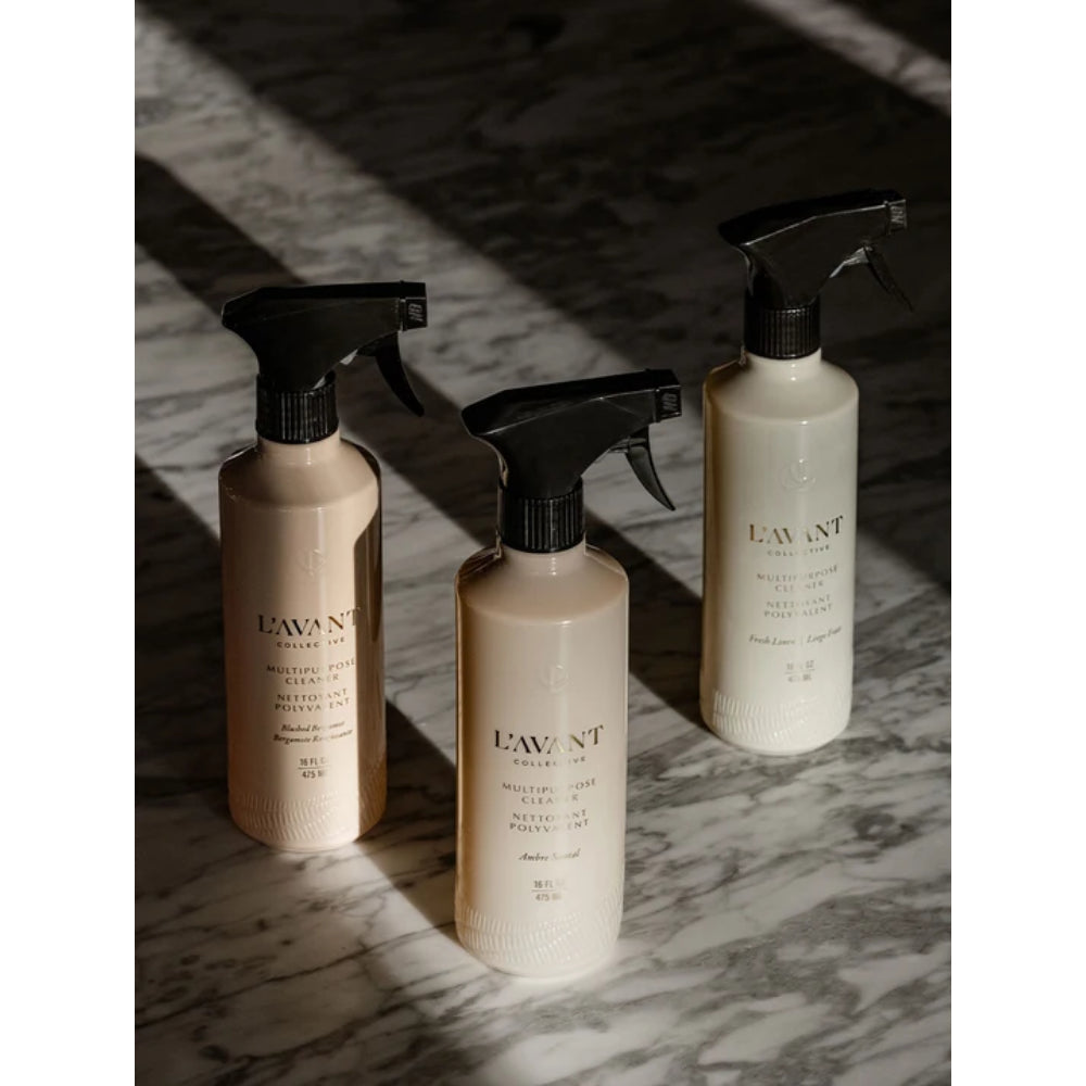 Three LAW NT Multi-Functional Spray bottles in natural beige and cream shades with black spray nozzles, arranged on a dark marble surface under dramatic diagonal shadows.