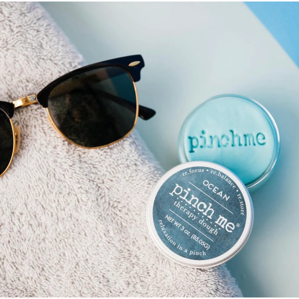 Two containers of 'pinch me' therapy dough with sunglasses on a towel.
