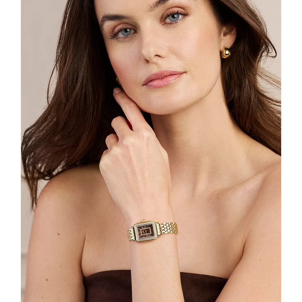 A woman wearing a gold-tone rectangular watch with a dark patterned dial and a gold mesh bracelet, shown in a close-up portrait.