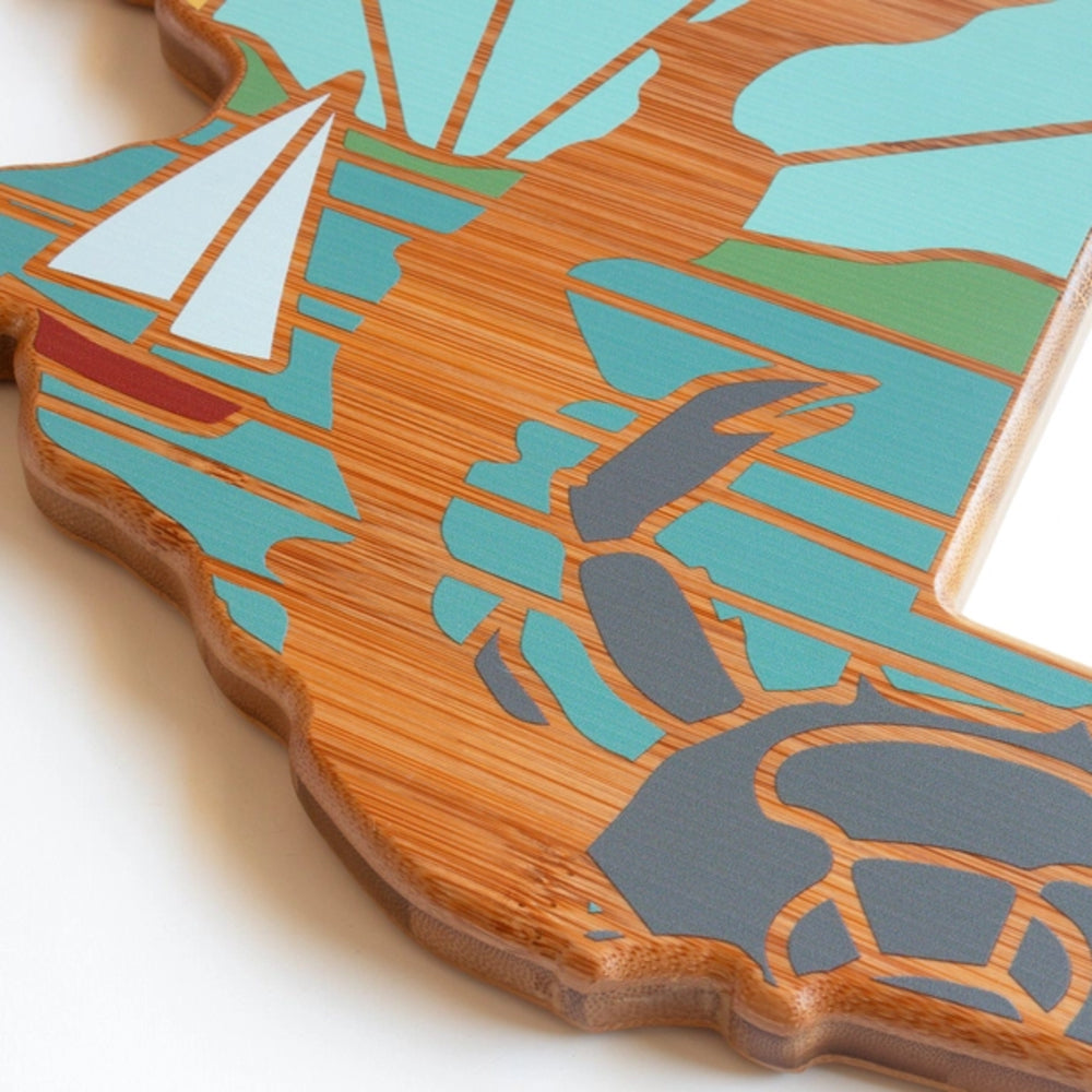 A close up photo of a decorative cutting board like a stylized map of Maryland and state flag with colorful patterns on a white background.