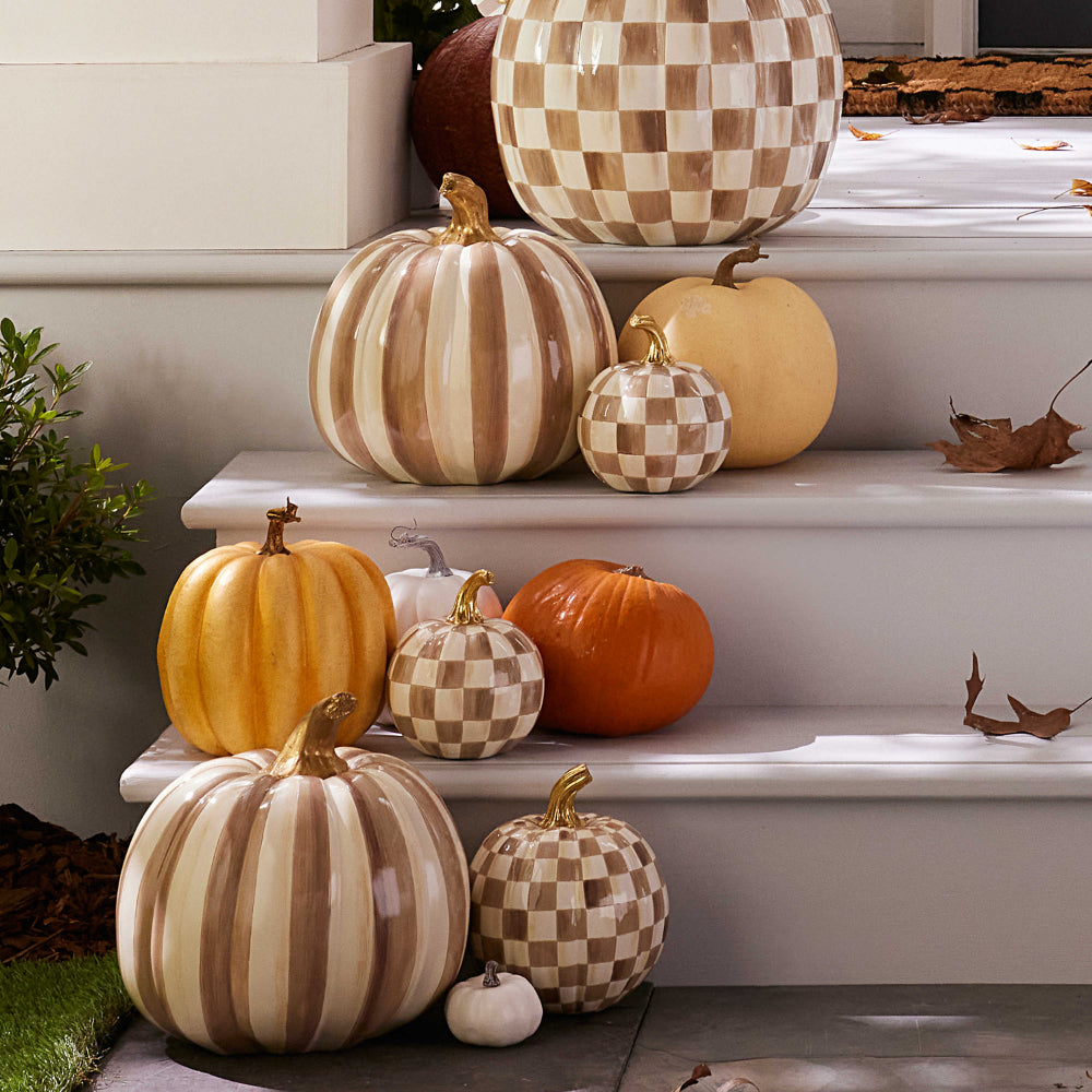  decorative pumpkins with checkered pattern and gold stem on a porch step with other orange and white pumpkins.