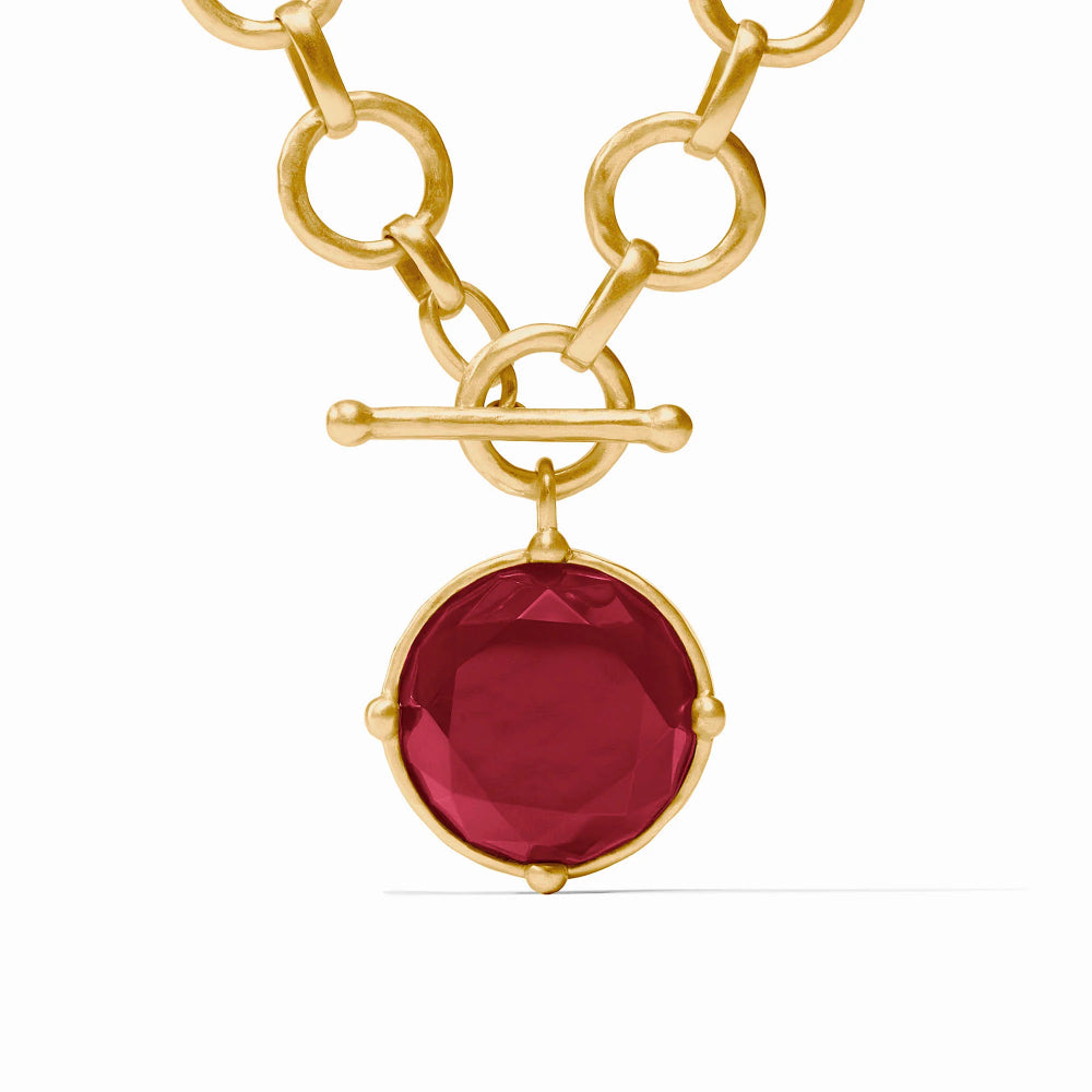 A gold chain necklace with a toggle clasp and a round faceted red gemstone pendant, shown on a clean white background.