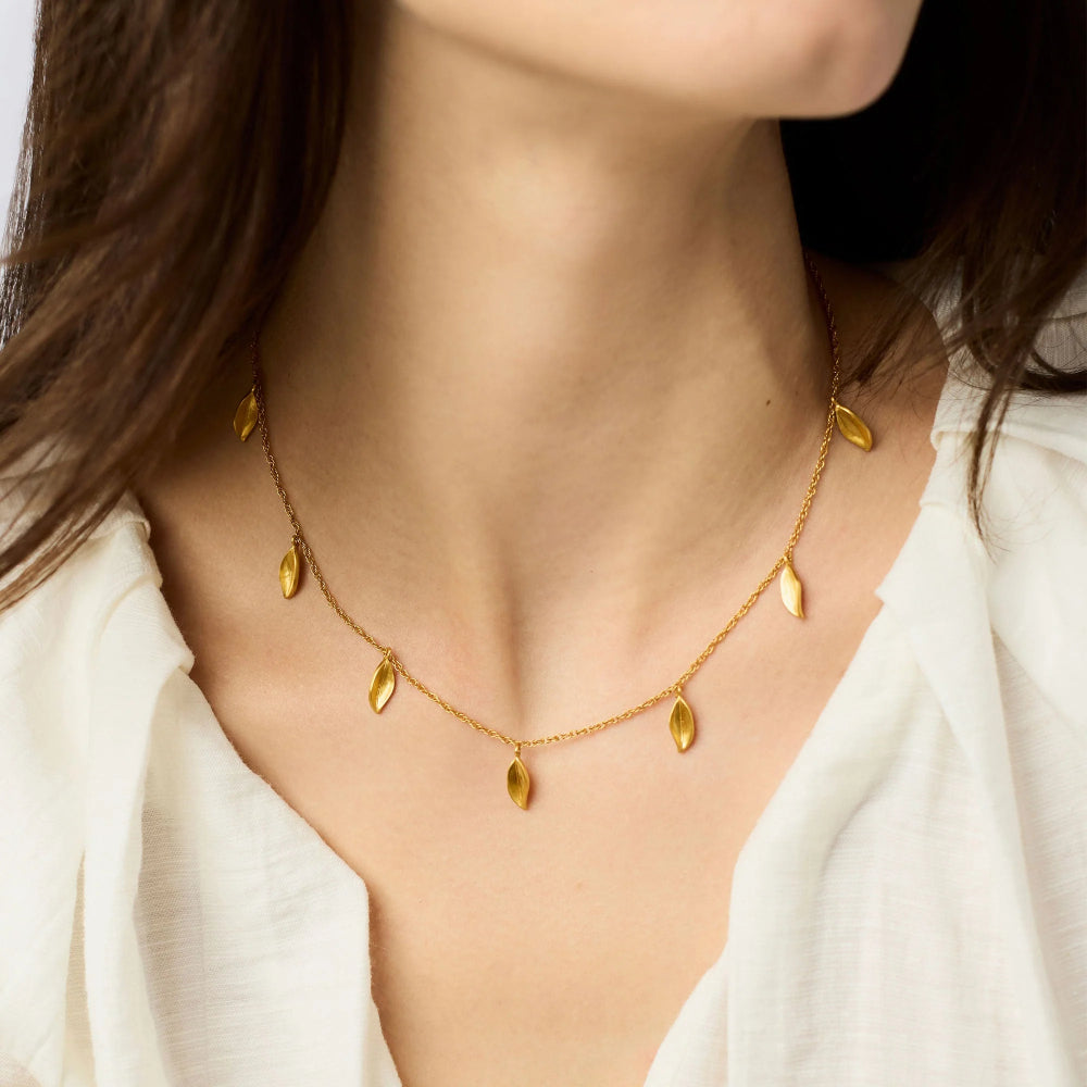 Gold necklace with leaf-shaped pendants on a person wearing a white top.