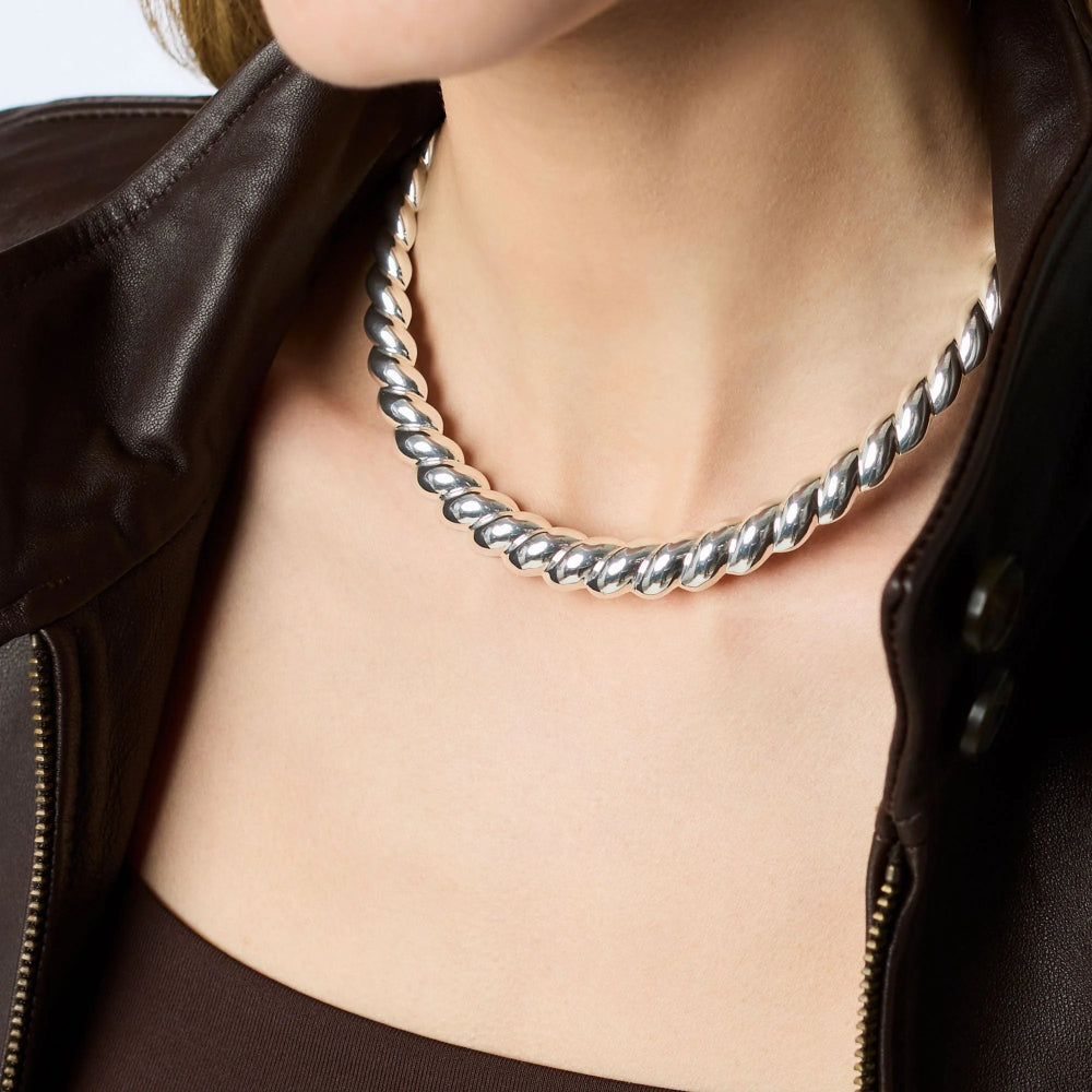 Close-up of a person wearing a silver twisted necklace with a blurred background