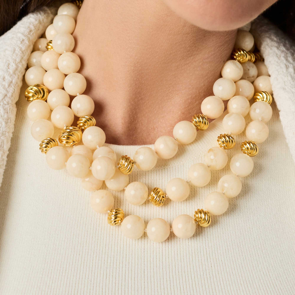 Close-up of a person wearing a beige beaded necklace with gold accents.