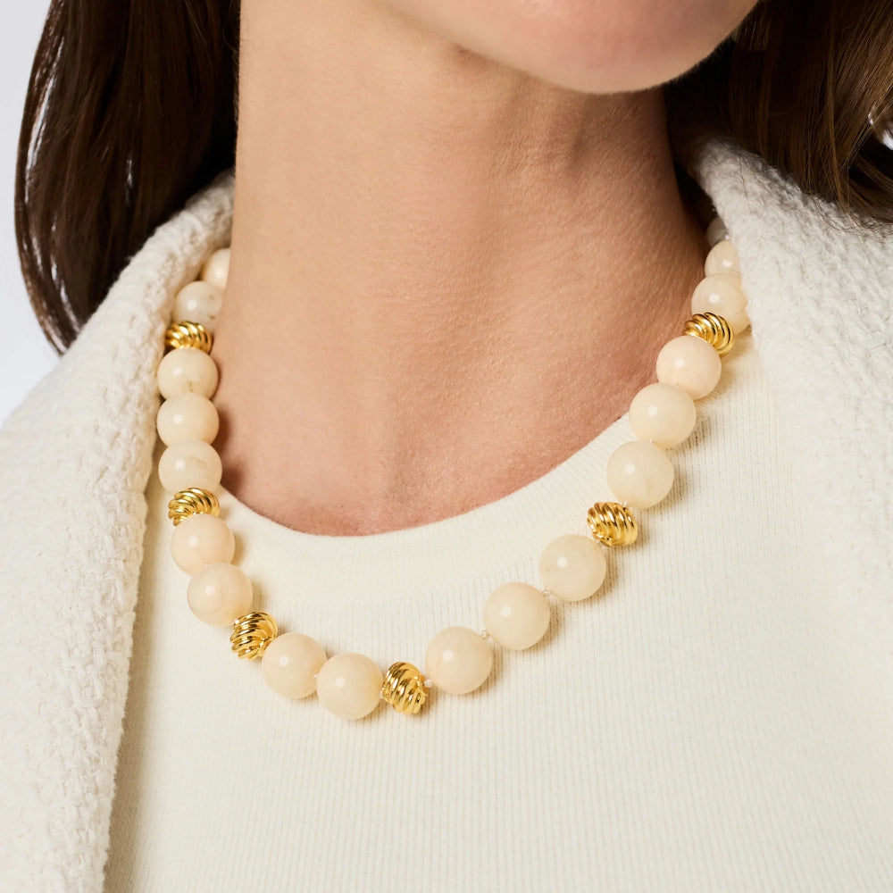 Necklace with ivory beads and gold accents worn by a person against a white background