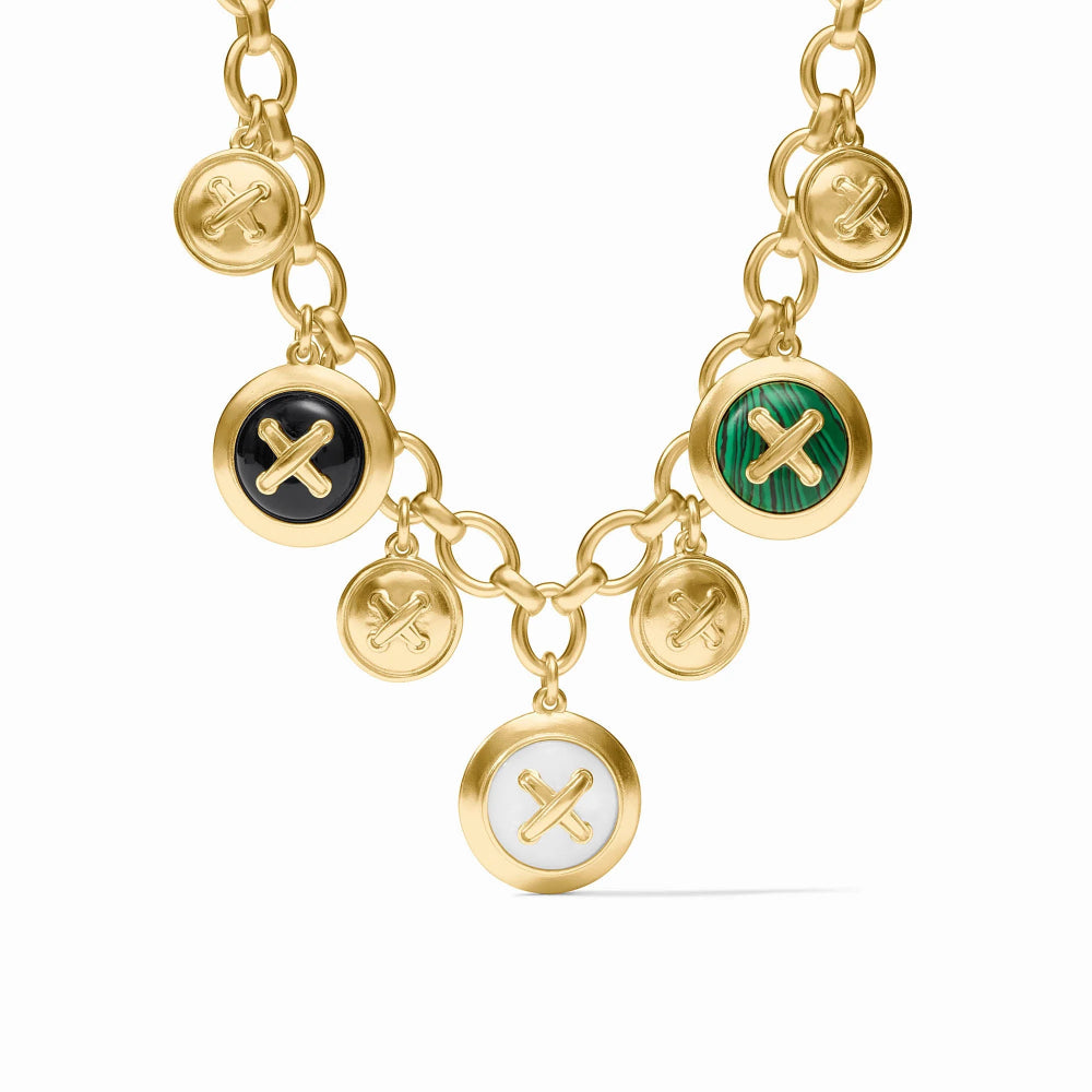A gold-tone charm necklace featuring multiple circular links with engraved 'X' logos, including two larger oval charms with black and green inlay and one larger oval pendant with a white inlay, shown on a clean white background.