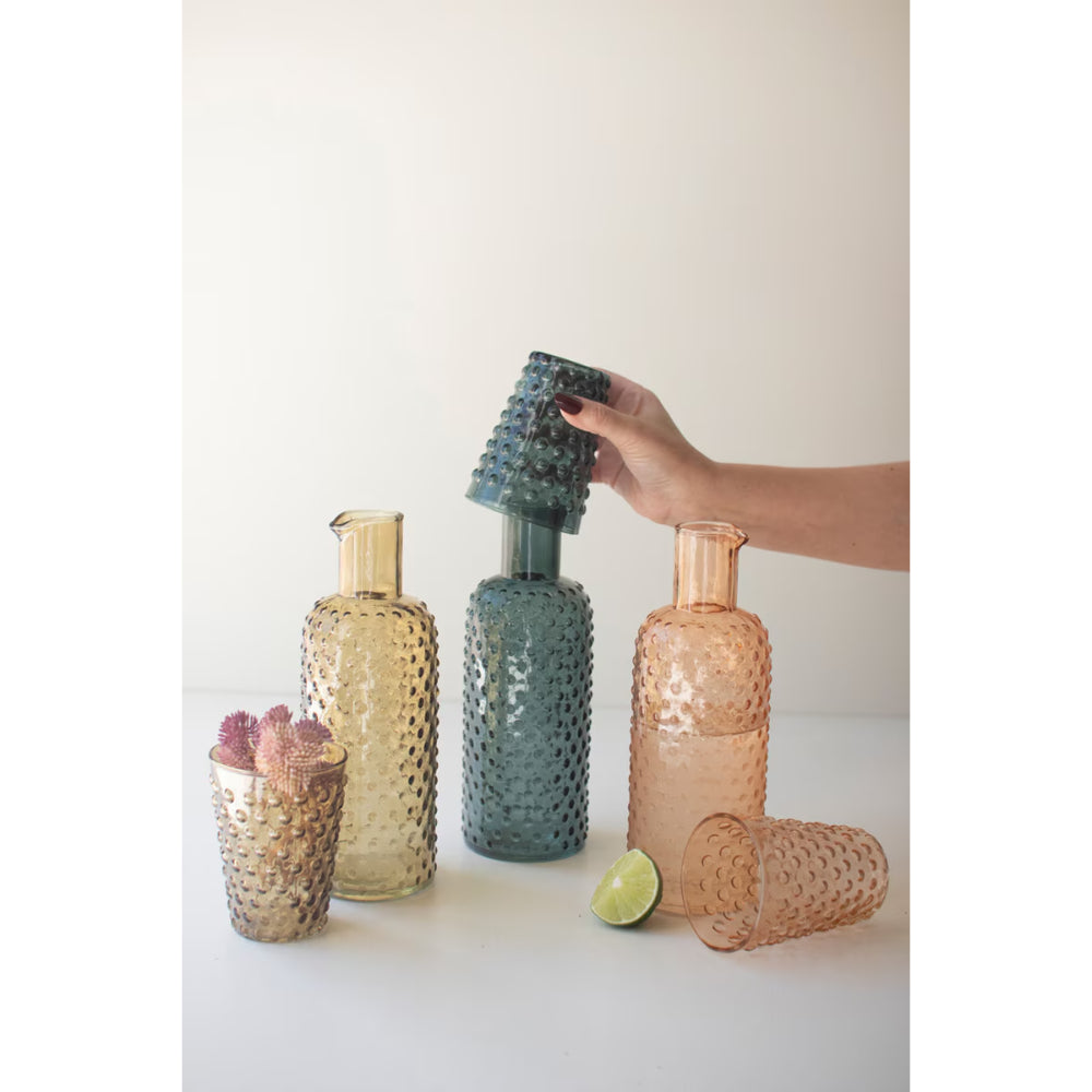 Hand holding a textured vase among other decorative vases on a light surface.