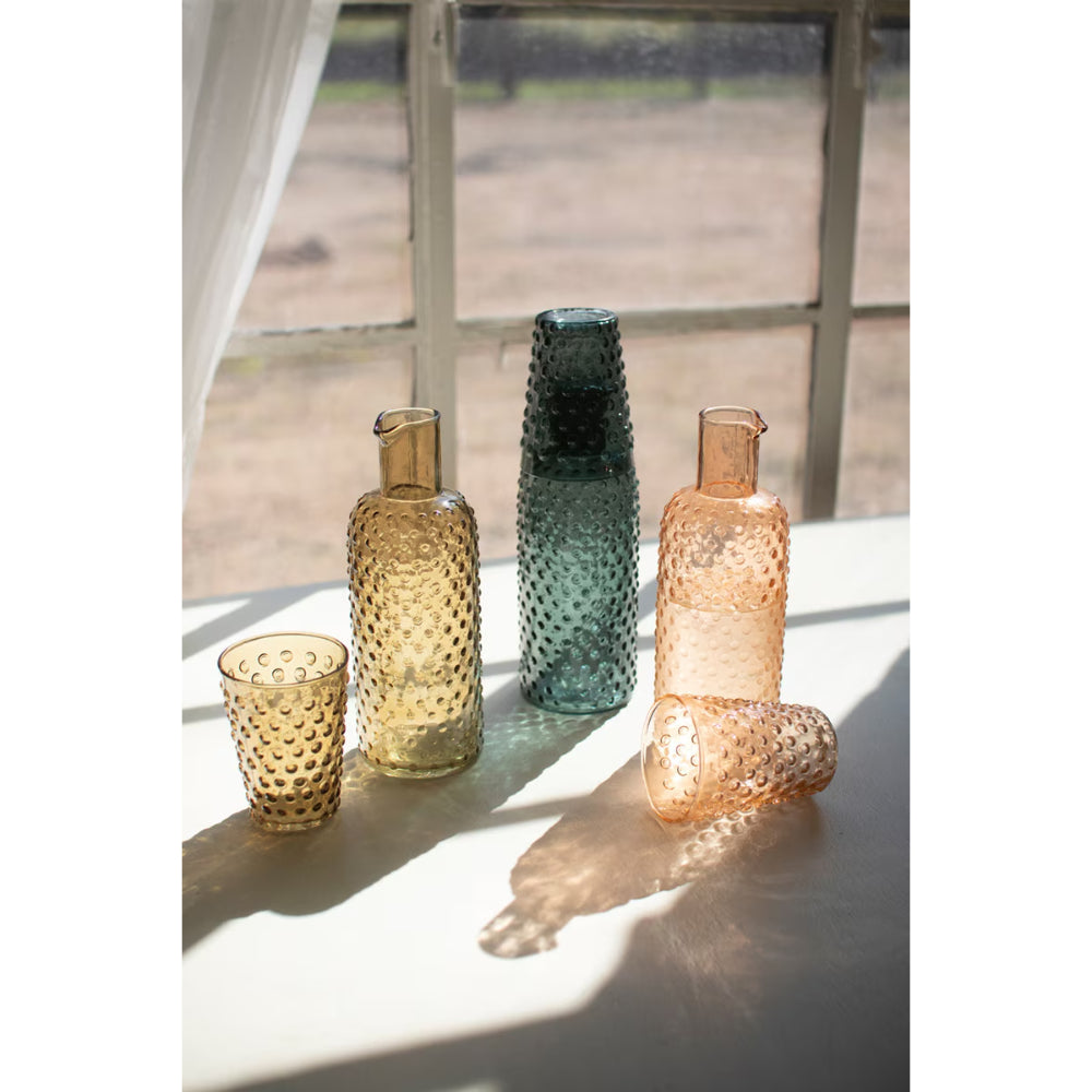Set of colorful glass vases on a reflective surface with a blurred outdoor background