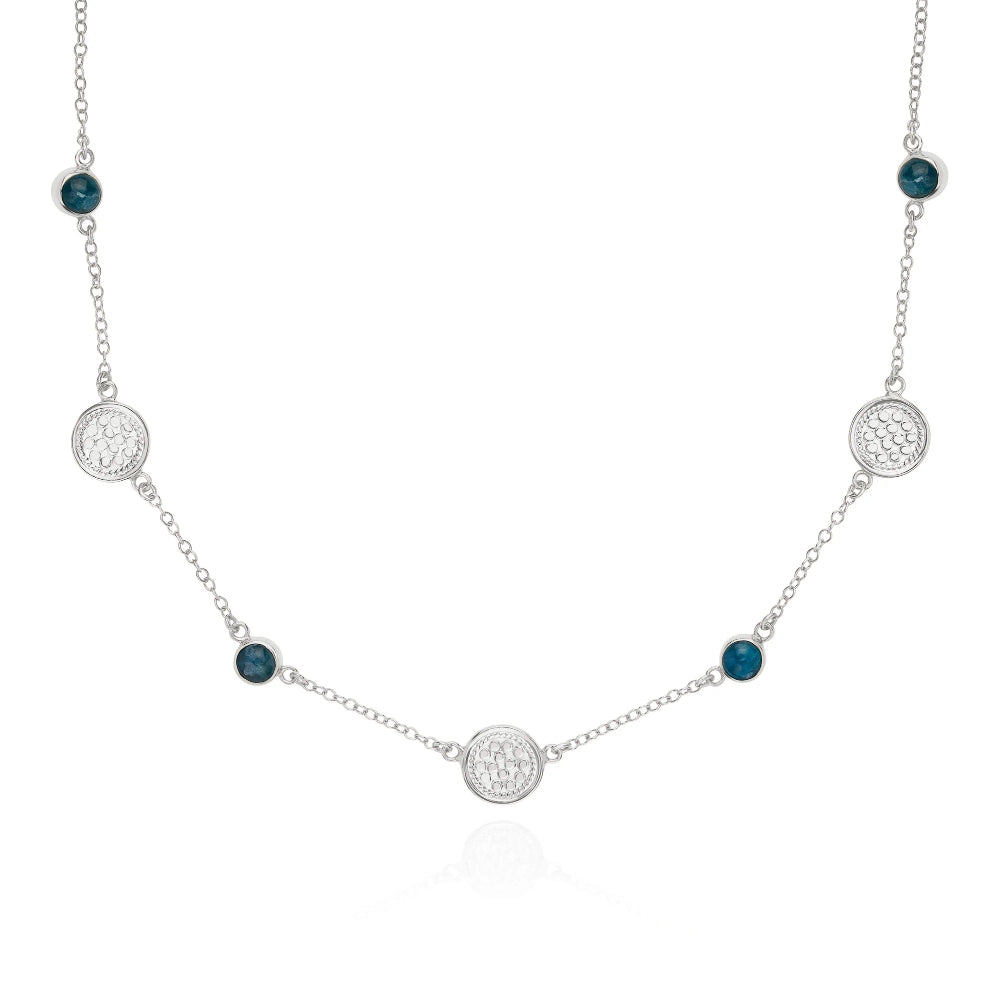 A silver chain necklace featuring textured circular disc charms and small round dark blue gemstone accents