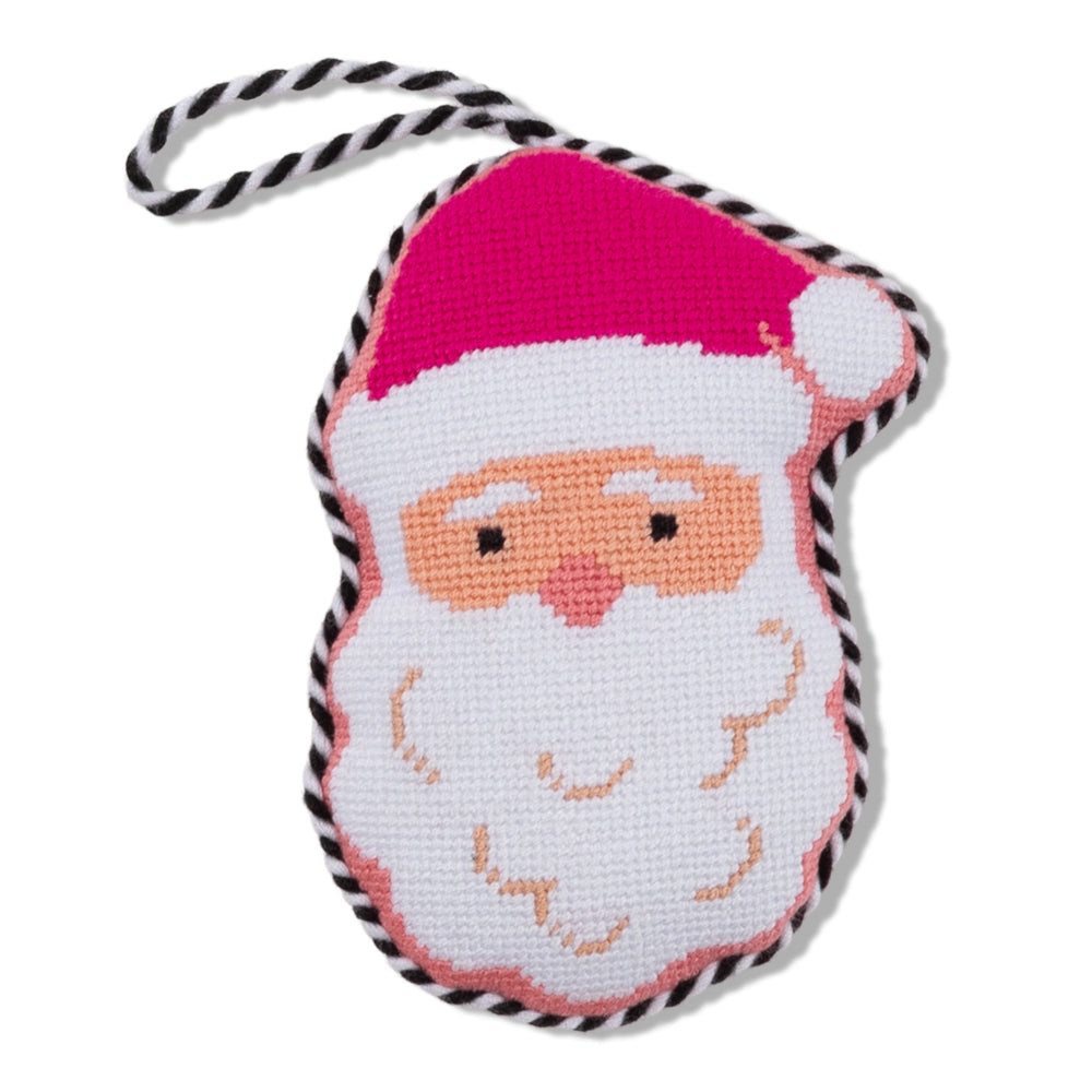 A handcrafted needlepoint ornament shaped like Santa's face, featuring a bright pink hat, white beard, peach skin, and a black-and-white braided hanging loop, shown on a clean white background.
