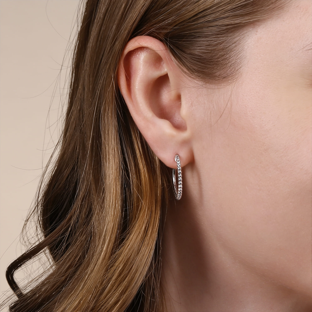 Close-up of an ear wearing a silver hoop earring with a neutral background