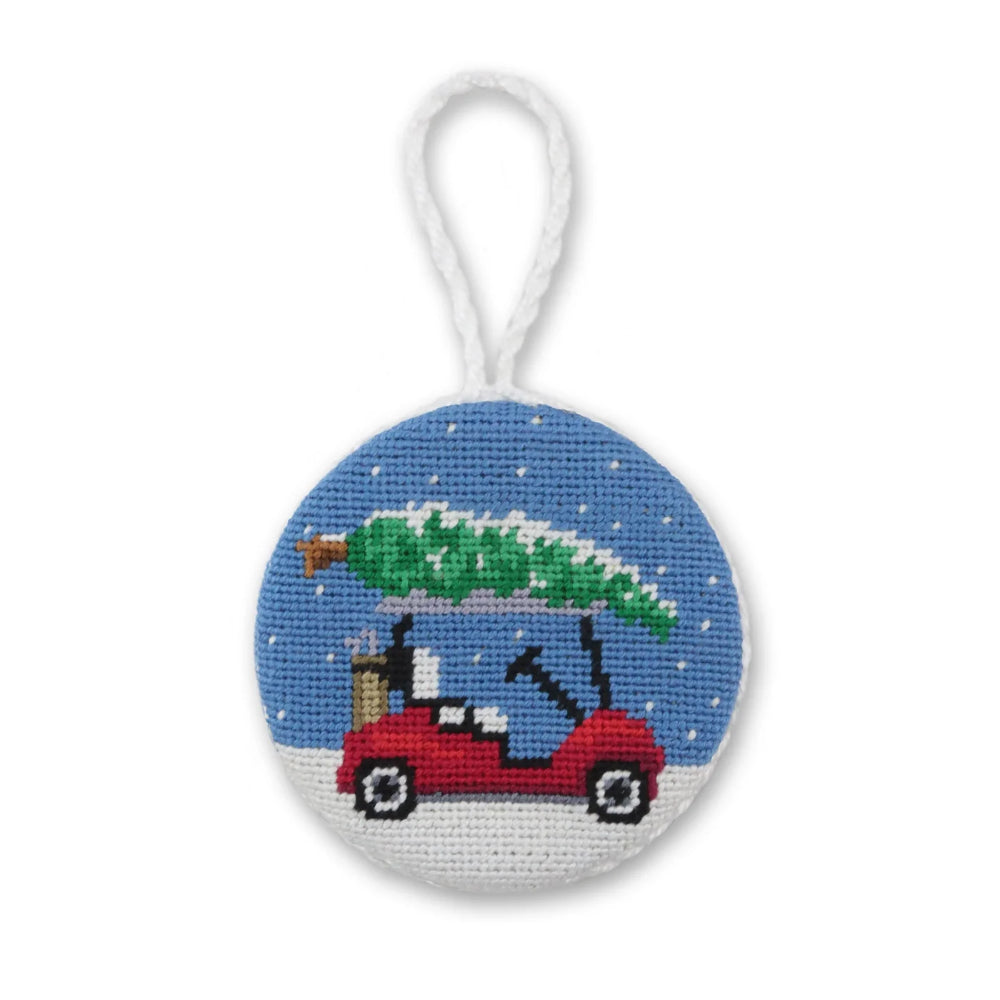Round needlepoint ornament with a red golf cart carrying a Christmas tree on a white background